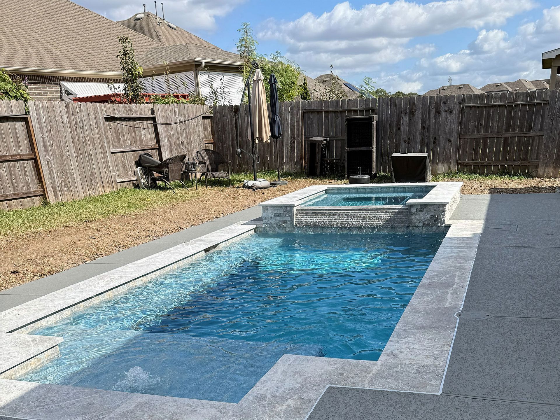 Backyard pool with blue water, raised spa, and wooden fence under a partly cloudy sky