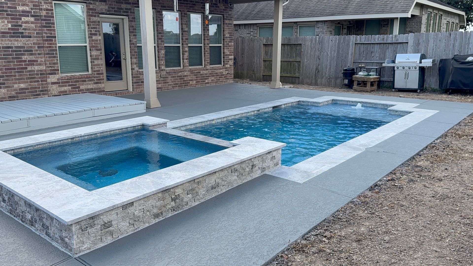 Backyard with a raised hot tub beside a rectangular blue swimming pool and stone patio
