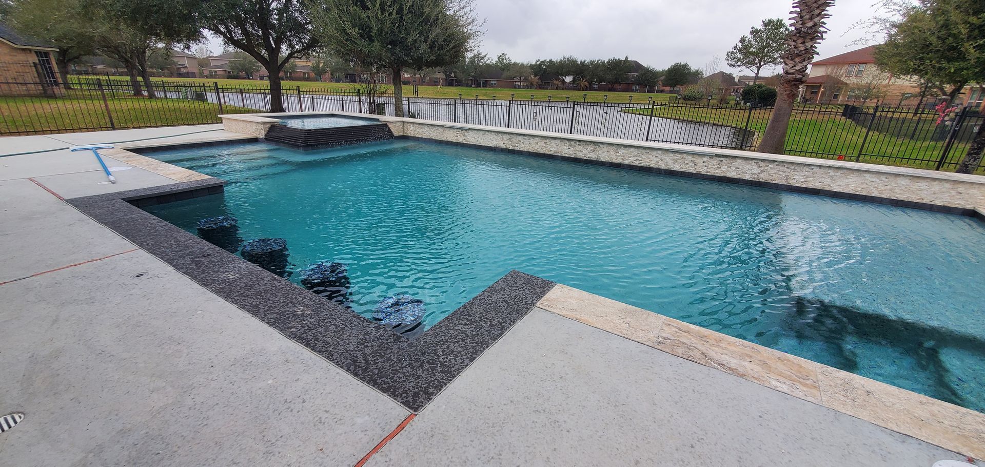 Outdoor swimming pool with turquoise water, concrete deck, and lounge chairs by a grassy park.
