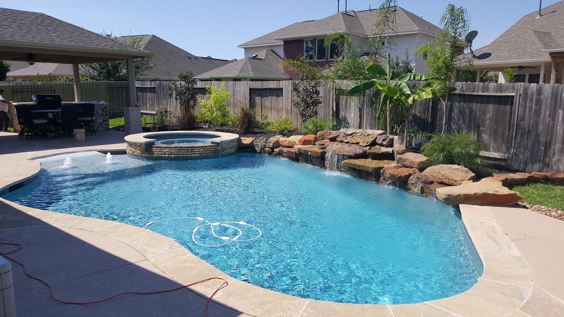 Backyard swimming pool with curved blue water, spa, rock landscaping, and patio in a suburban yard