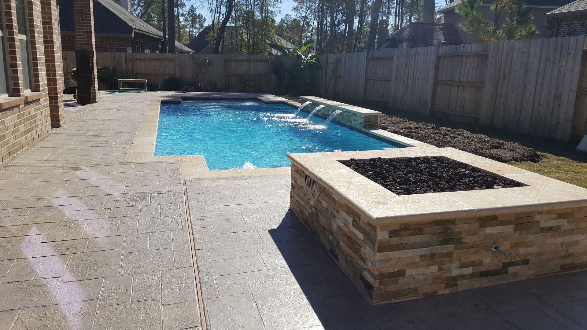 Backyard swimming pool with stone patio and raised planter box under a sunny sky