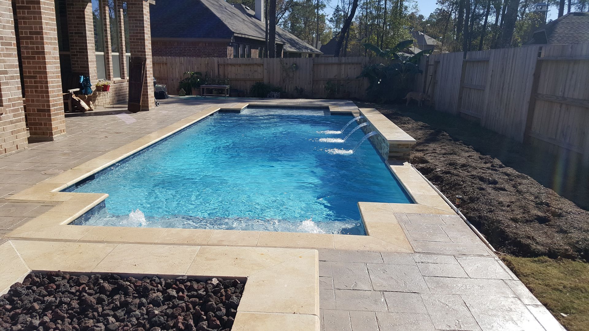 Backyard swimming pool beside a stone patio and fence on a sunny day