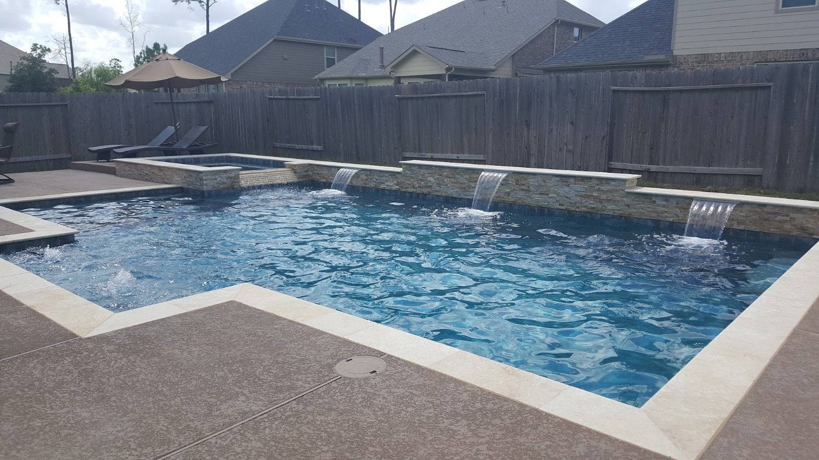 Backyard swimming pool with blue water, white coping, and surrounding wooden privacy fence.