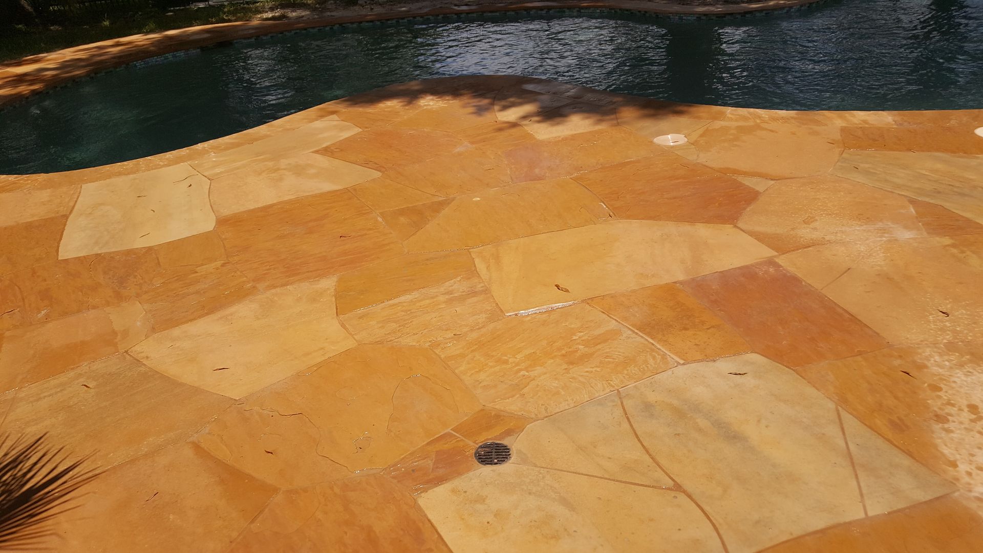 Orange-tiled pool deck beside dark water, with a few drains visible
