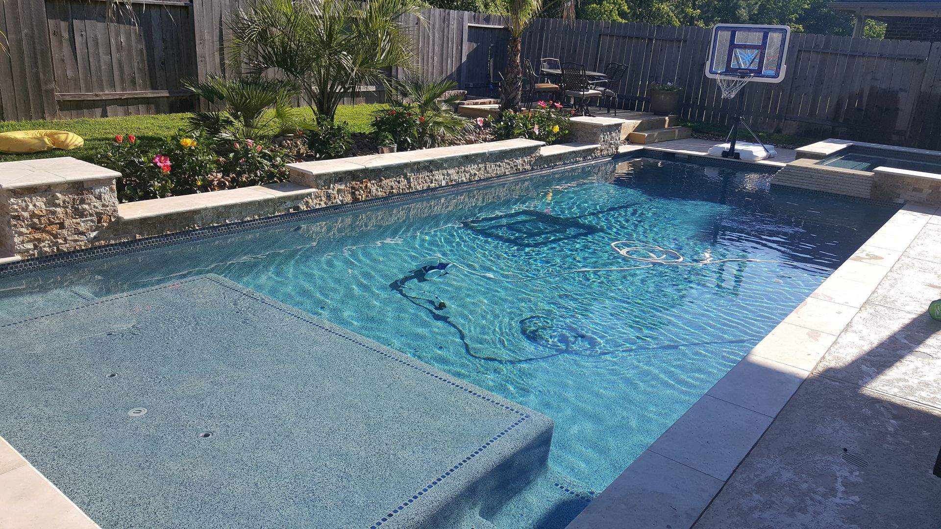 Backyard swimming pool with clear blue water and stone patio in bright sunlight