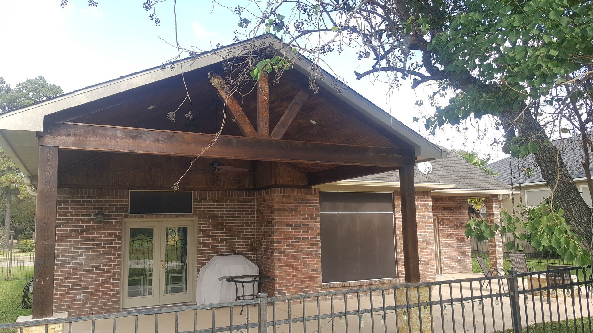 Brick house with a gabled porch and white windows behind a metal fence, shaded by trees