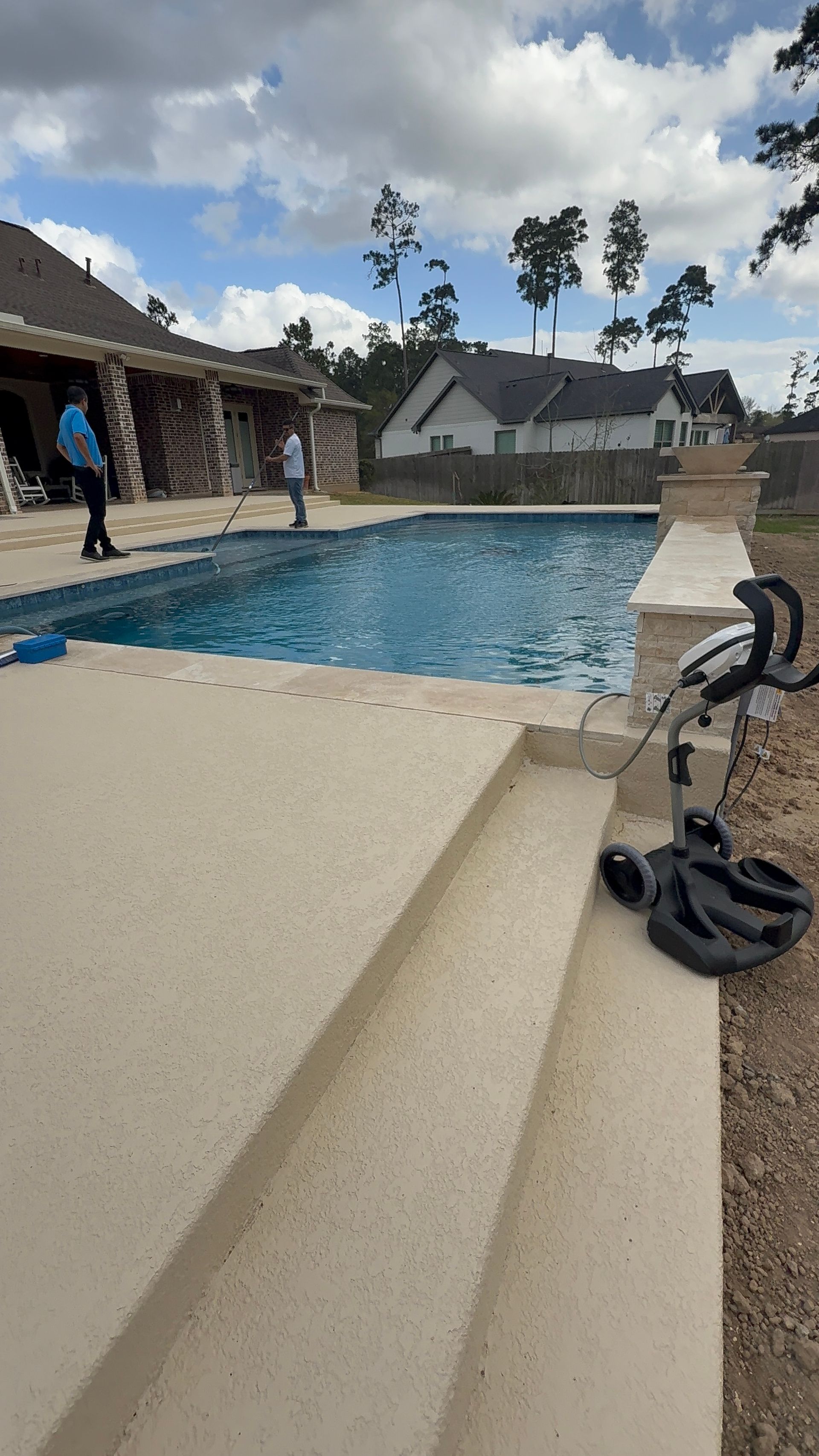 Backyard pool with beige steps, lounge chair, patio, and cloudy sky