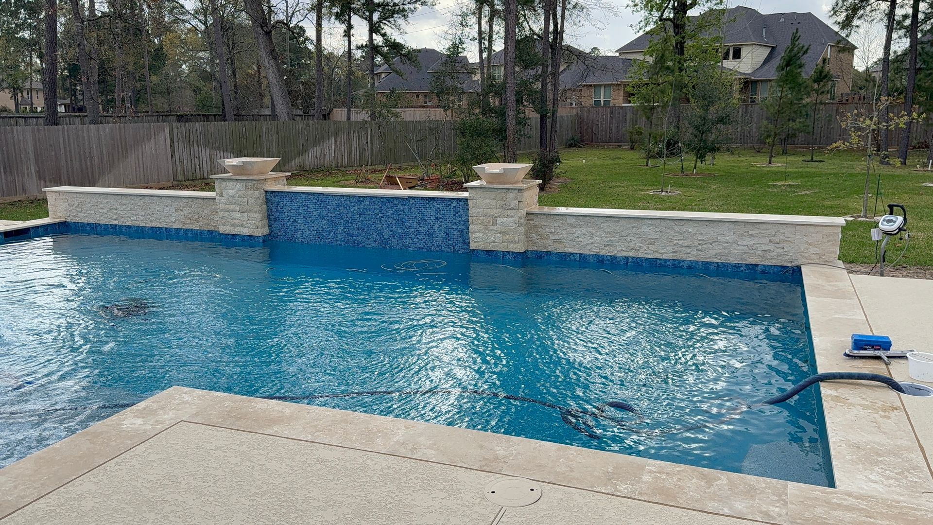 Backyard swimming pool with blue water, stone waterfall, and patio under an overcast sky