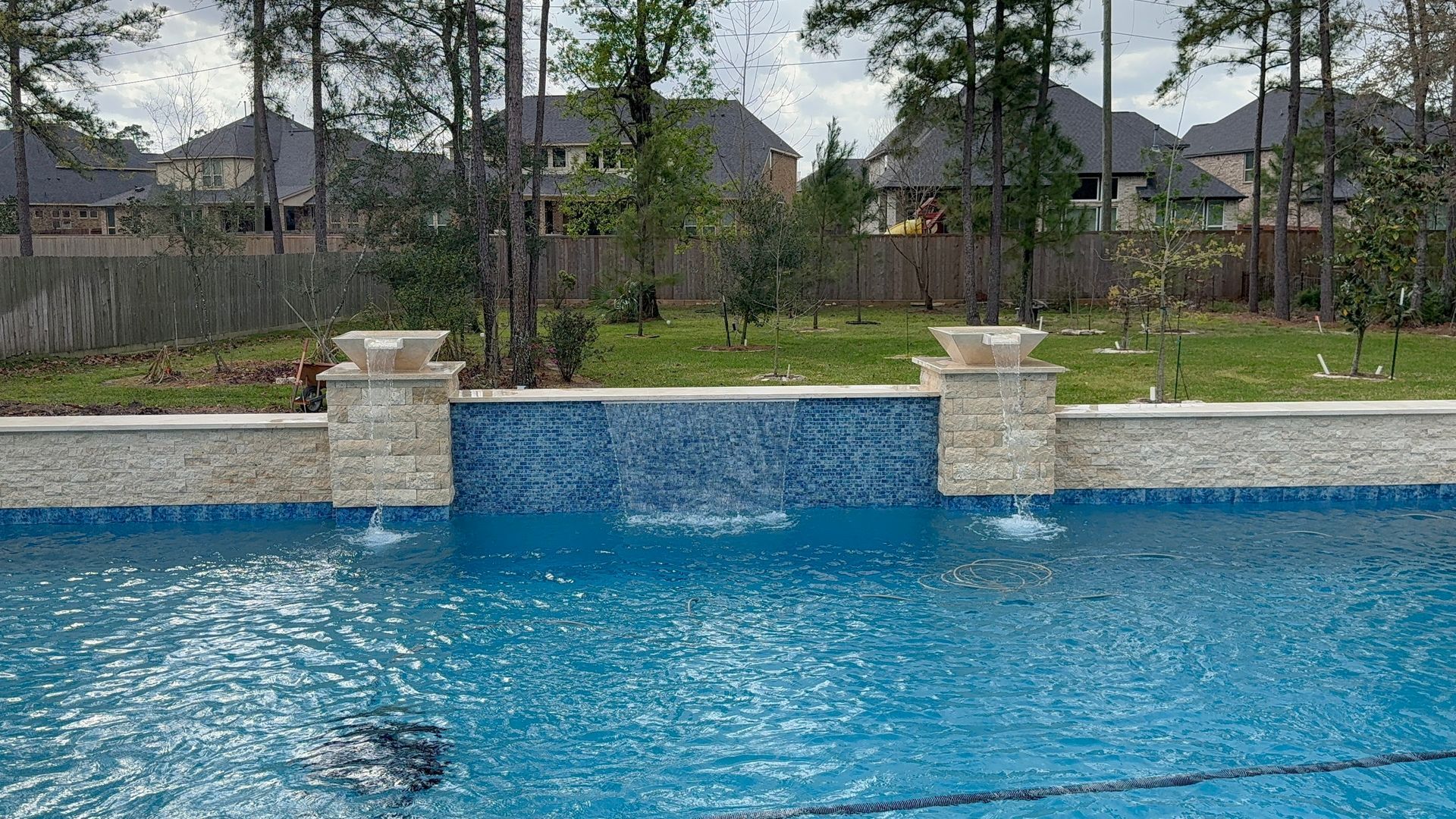 Blue swimming pool with stone waterfall feature and houses in the background