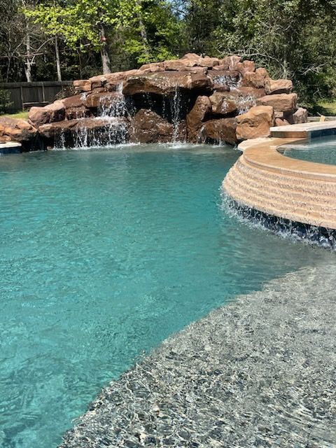 Turquoise pool with rock waterfall and curved stone spa edge in a lush backyard setting