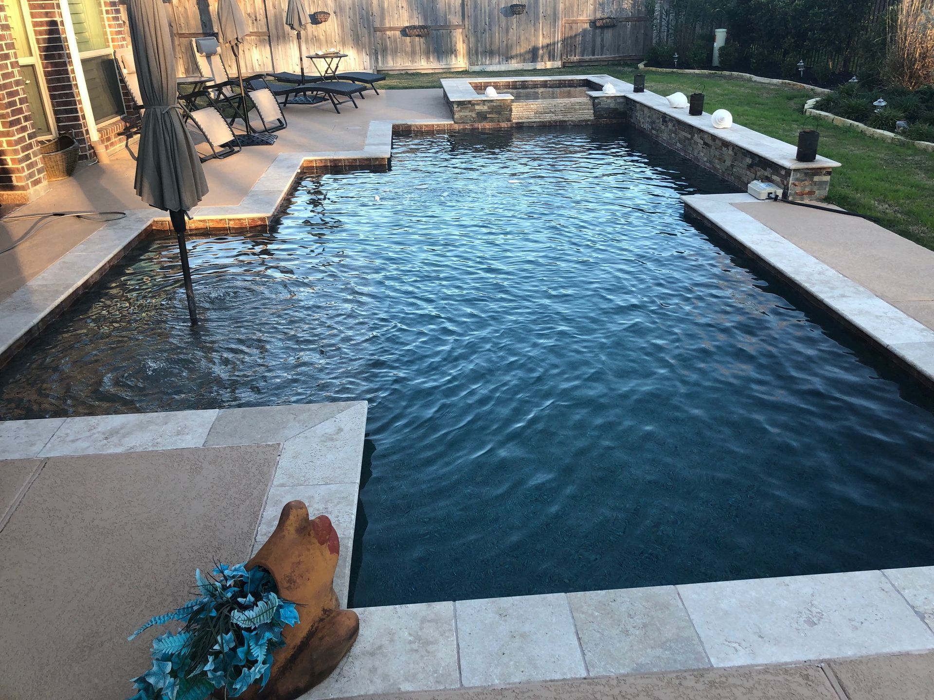 Backyard swimming pool with stone decking and a person’s feet at the edge.