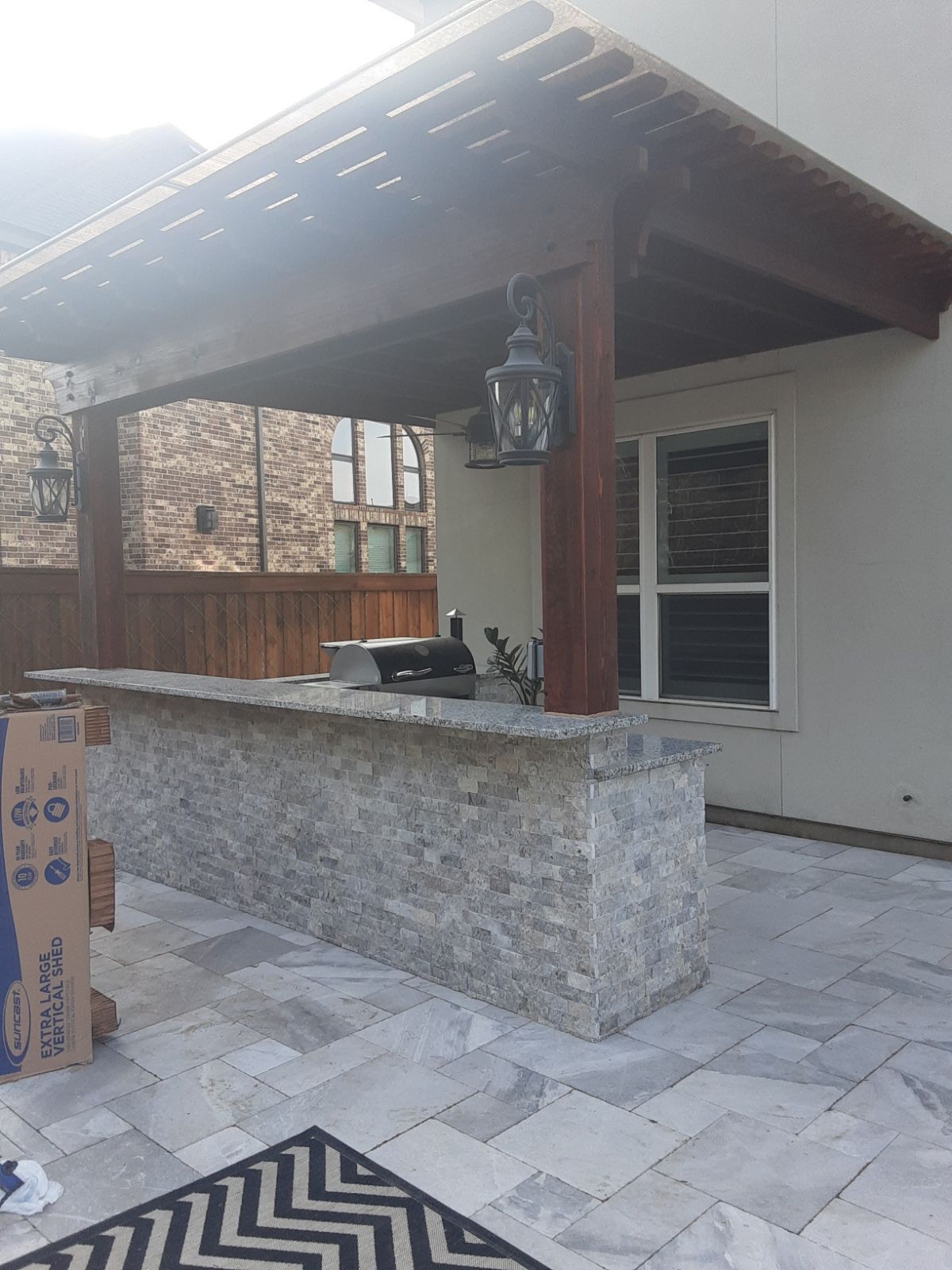 Covered outdoor patio with stone bar, hanging lantern, tiled floor, and white house wall under a wooden roof