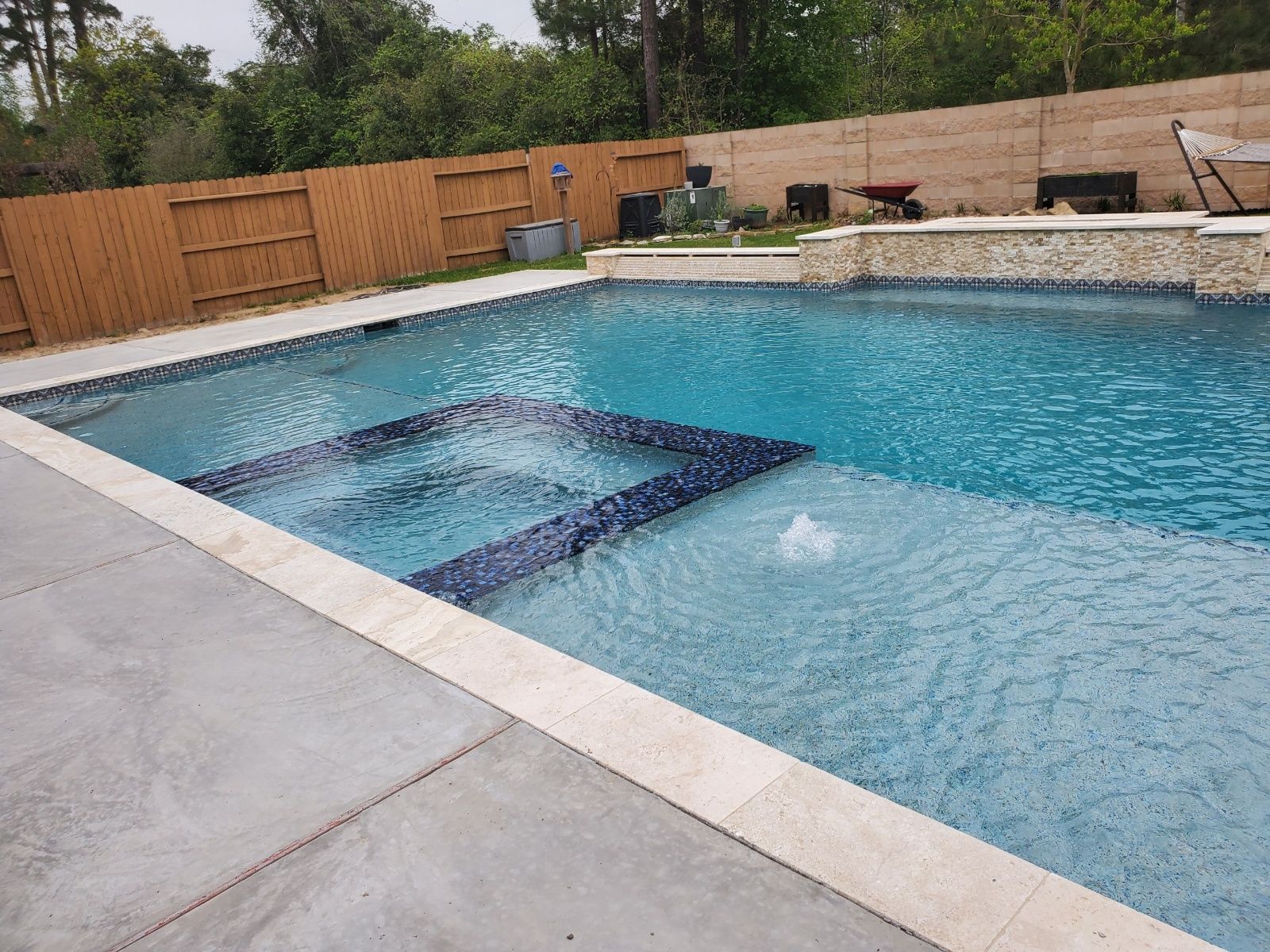 Backyard swimming pool with clear blue water, a submerged bench, and a wooden privacy fence around it