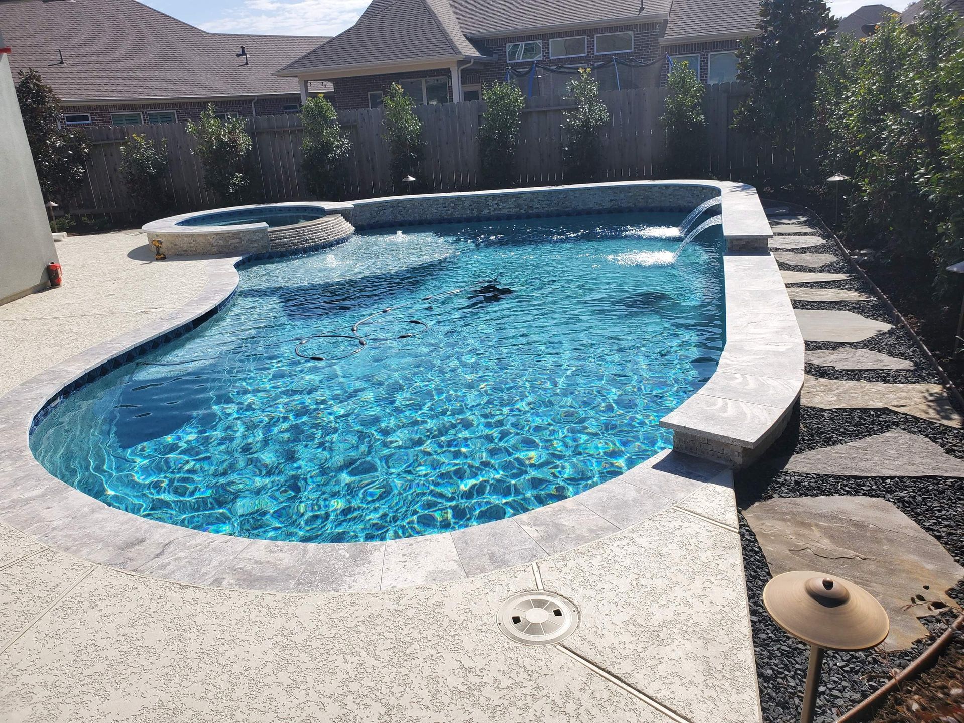 Backyard swimming pool with blue water, white deck, and stone edging under a sunny sky