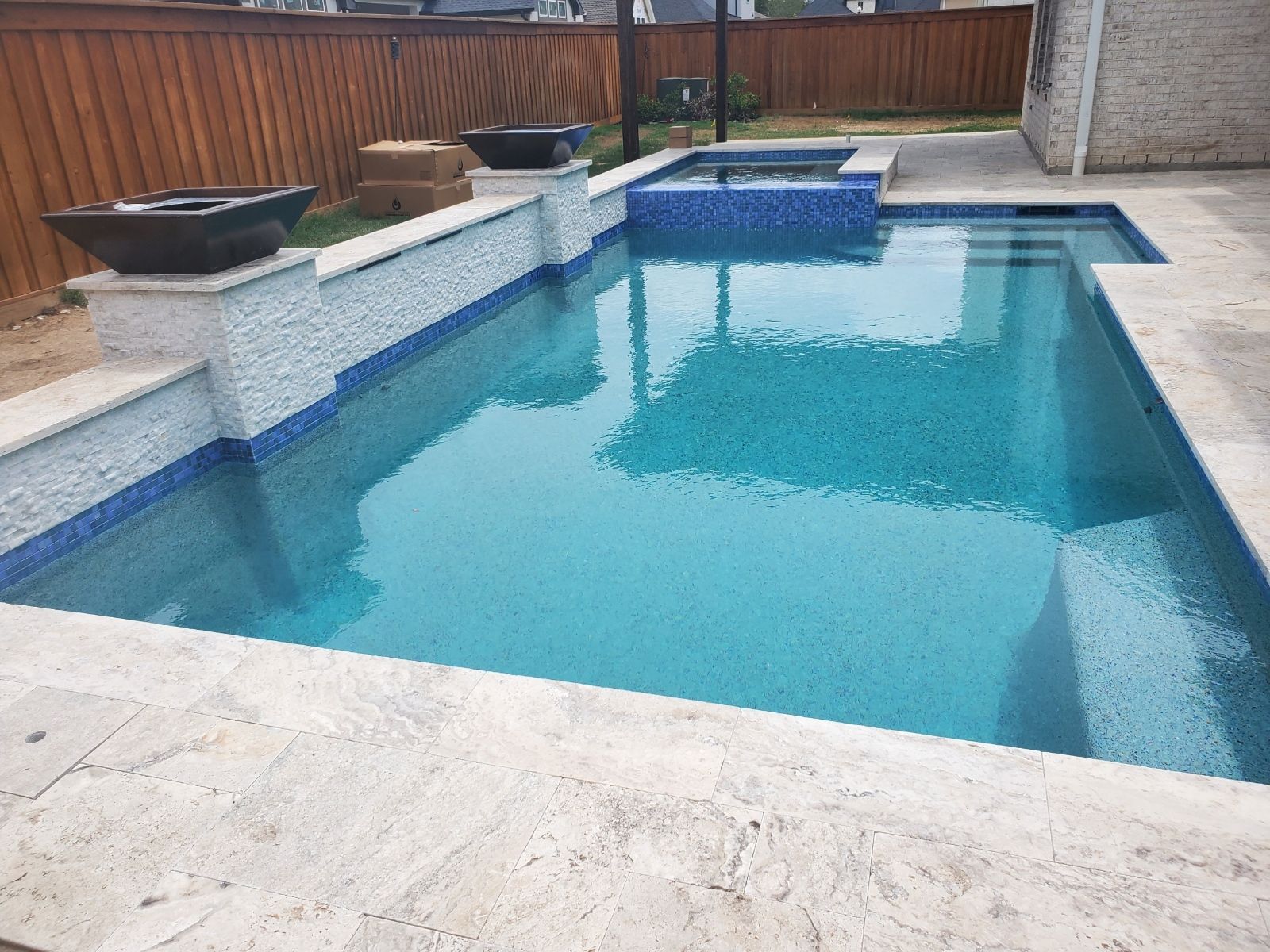 Backyard swimming pool with blue water, white stone deck, and a wooden fence