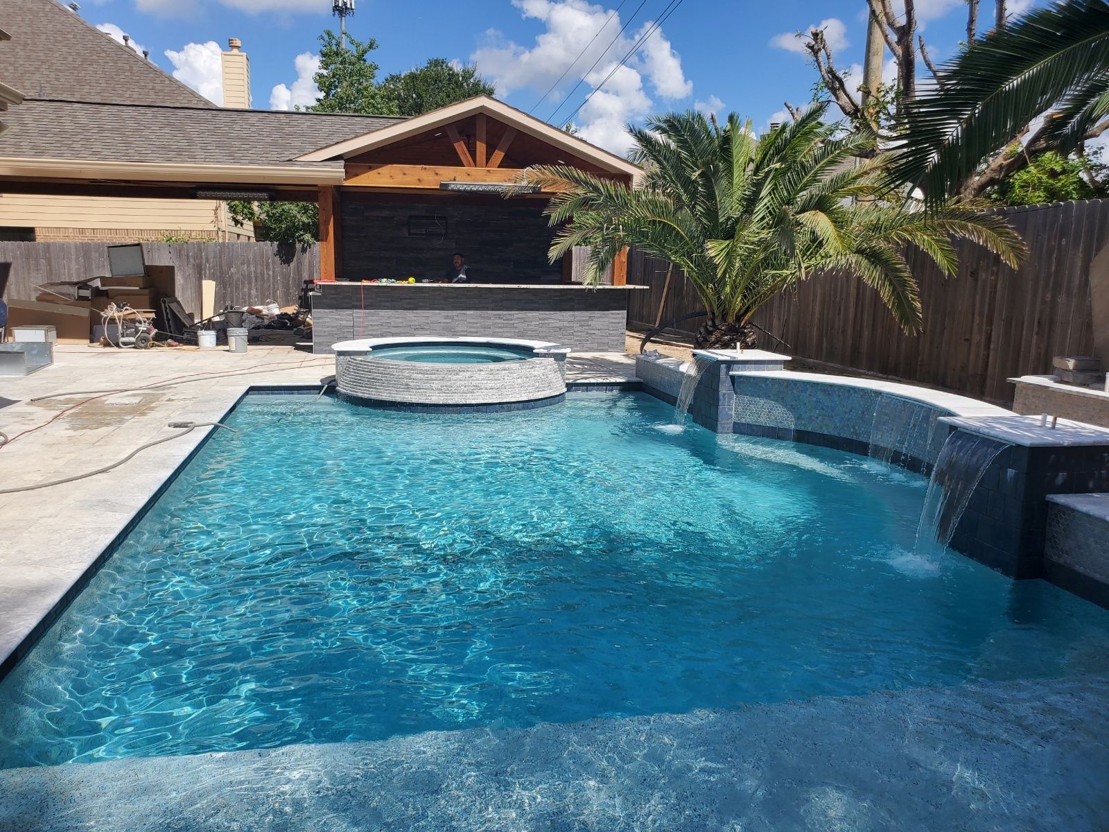 Backyard swimming pool with a raised hot tub, palm trees, and a covered patio under a sunny sky
