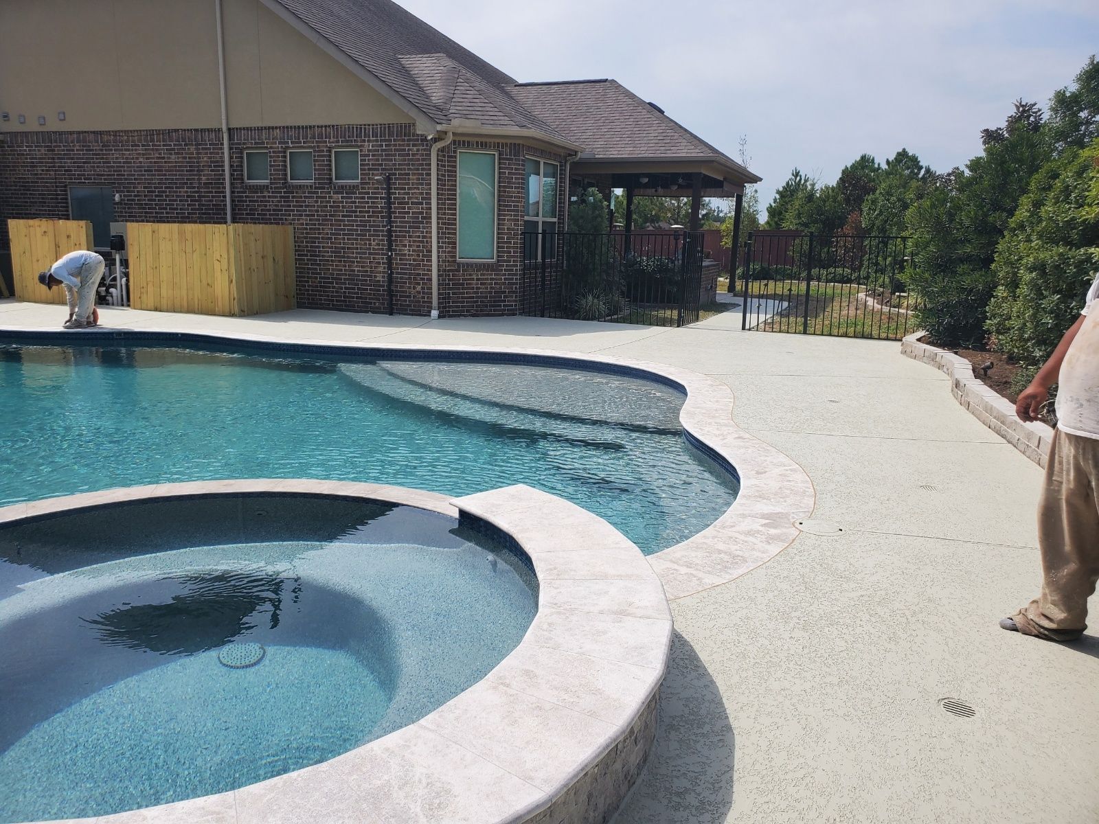 Backyard pool with curved spa, white deck, and a brick house in the background