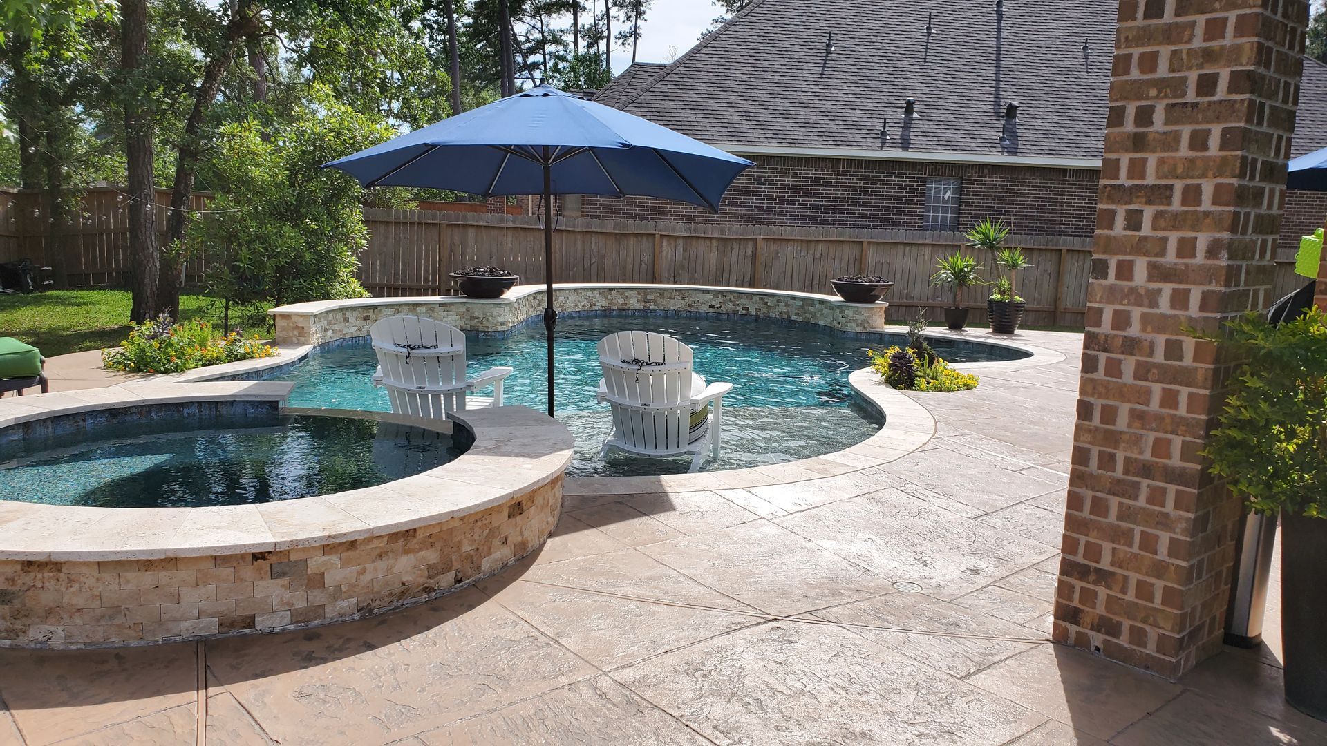 Backyard patio with a swimming pool, hot tub, blue umbrella, and brick house siding