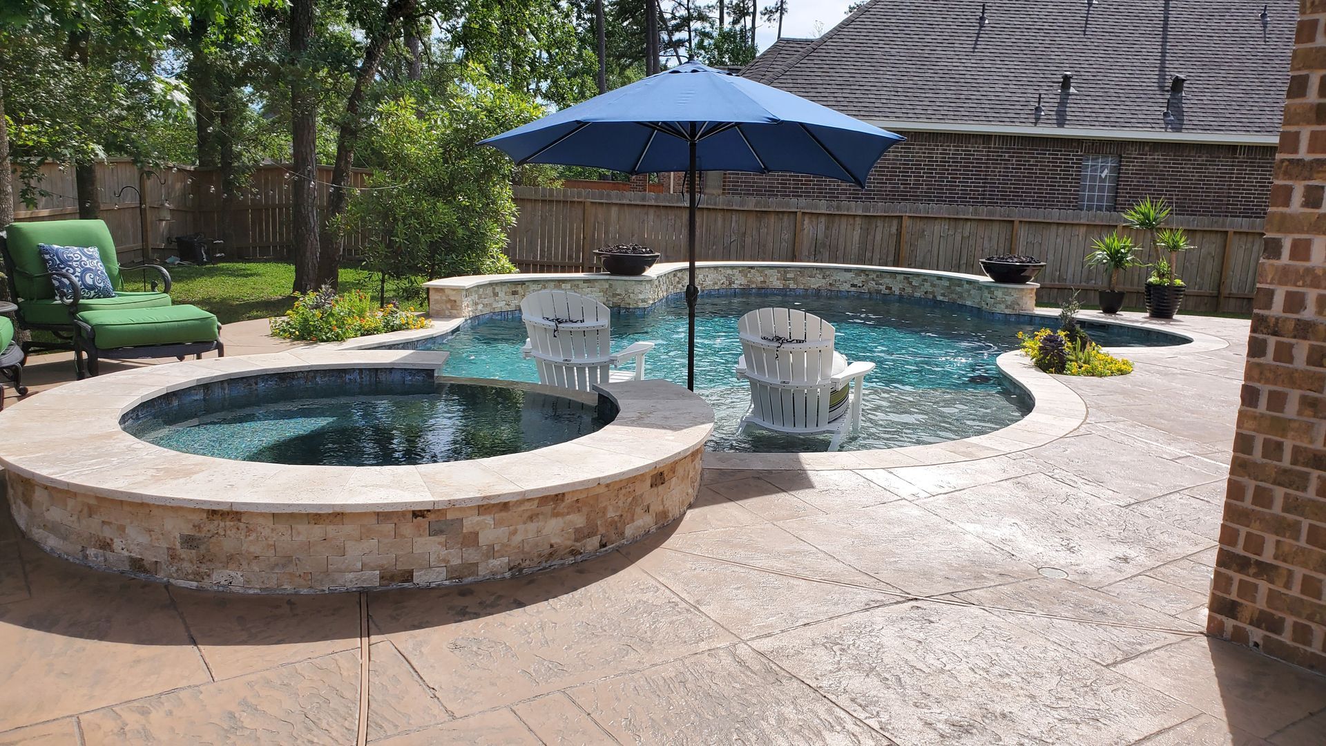 Backyard swimming pool with stone spa, blue umbrella, lounge chairs, and brick patio