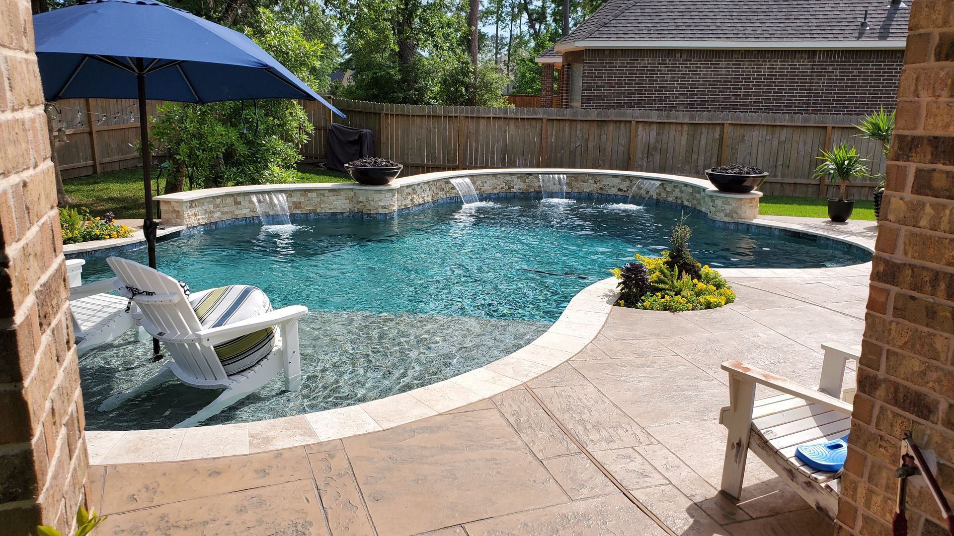Backyard pool with turquoise water, lounge chairs, blue umbrella, and a stone patio surrounded by greenery