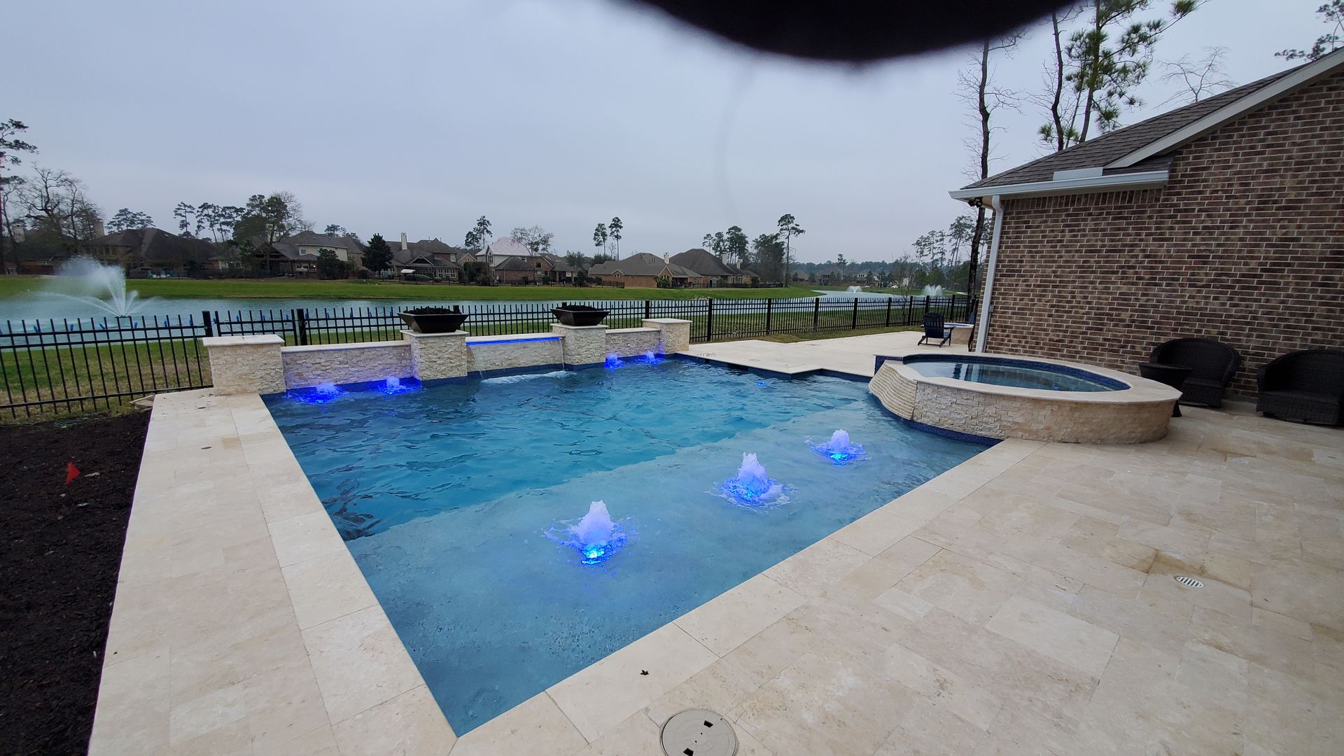 Backyard pool with blue-lit water, stone patio, and a raised spa beside a palm tree.