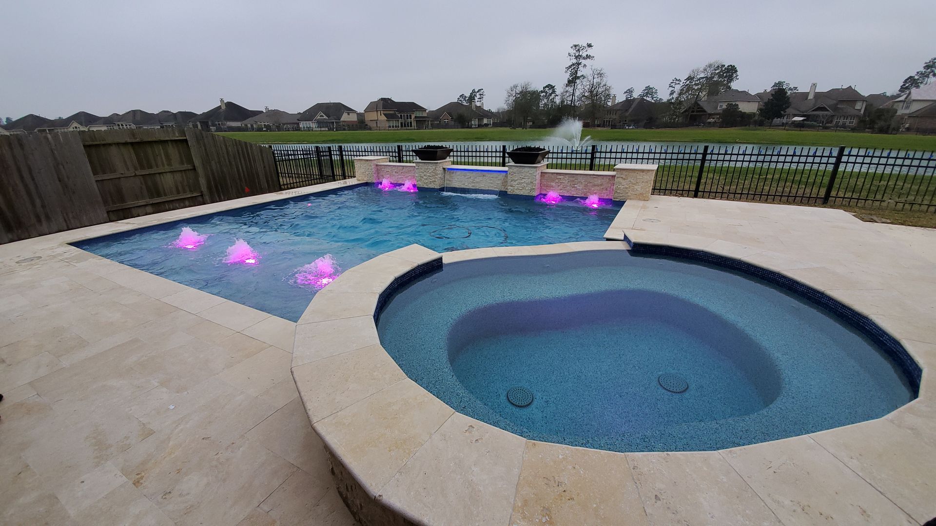 Backyard pool with a round hot tub in the foreground and purple lights glowing in the water at dusk