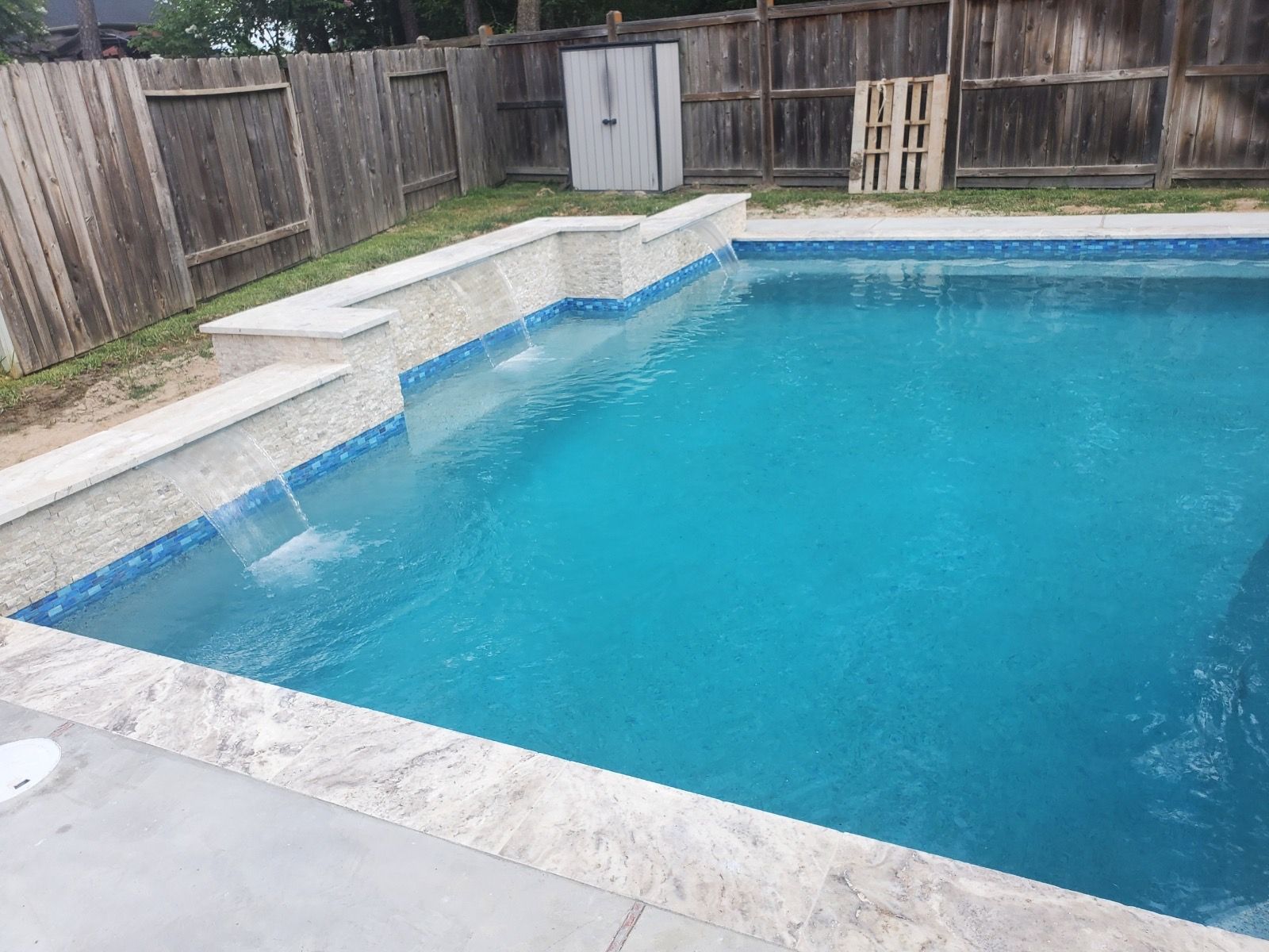 Backyard swimming pool with clear blue water, concrete deck, and wooden fence surround