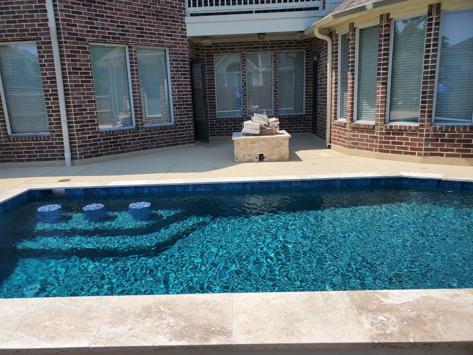 Backyard patio with a blue-tiled swimming pool in front of a brick house and sliding glass doors