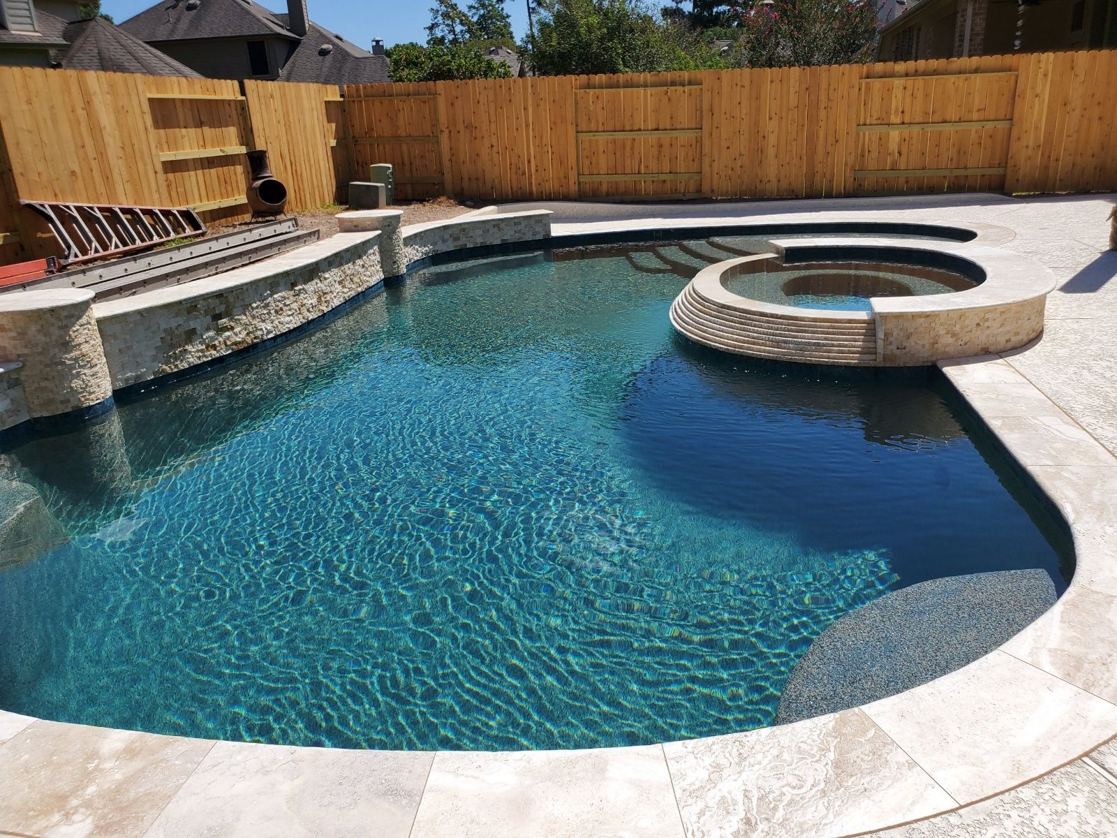 Backyard swimming pool with a curved stone edge and built-in circular spa under bright sunlight