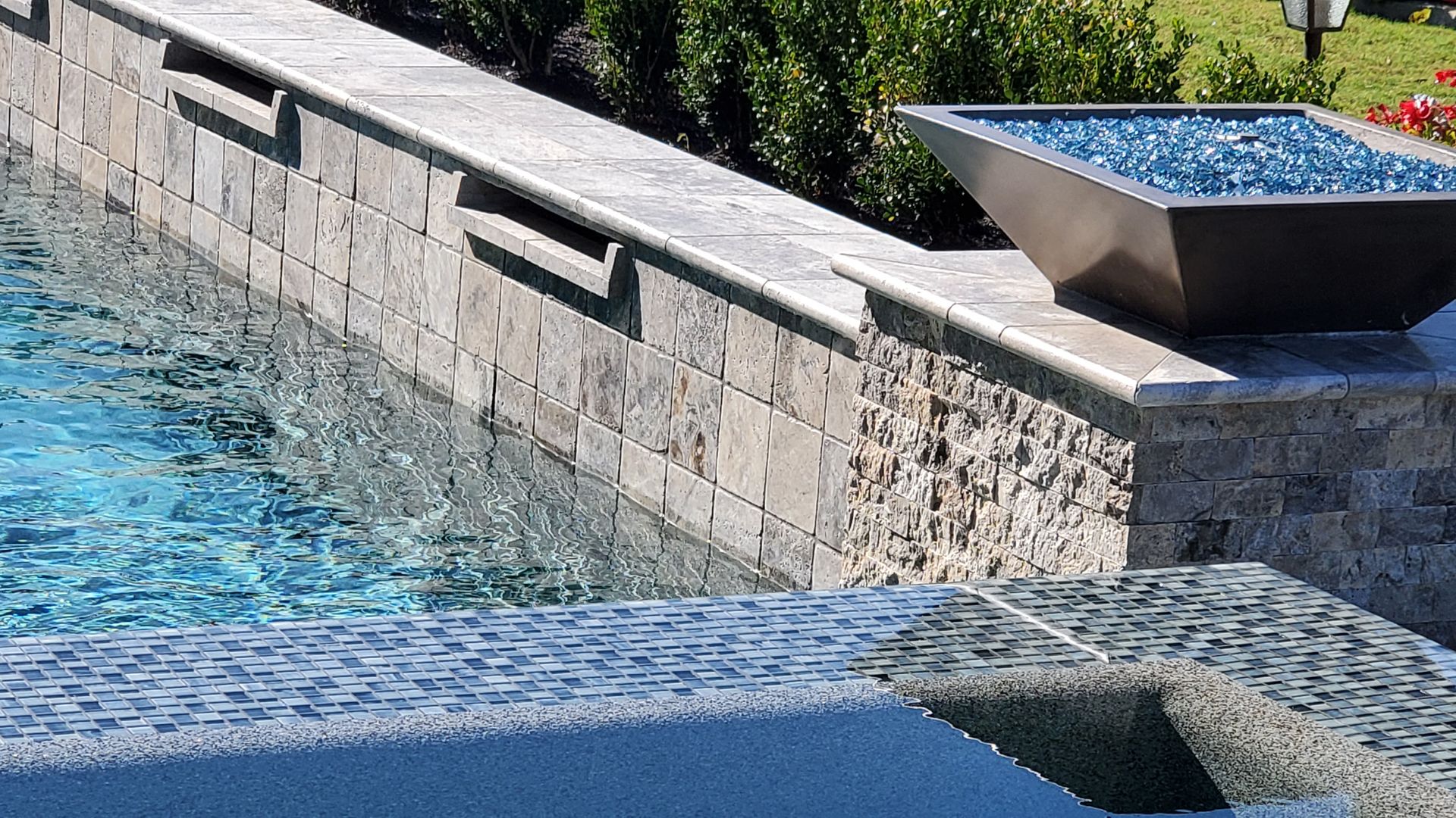 Stone pool edge with blue water and a built-in basin fountain spilling onto a tiled ledge