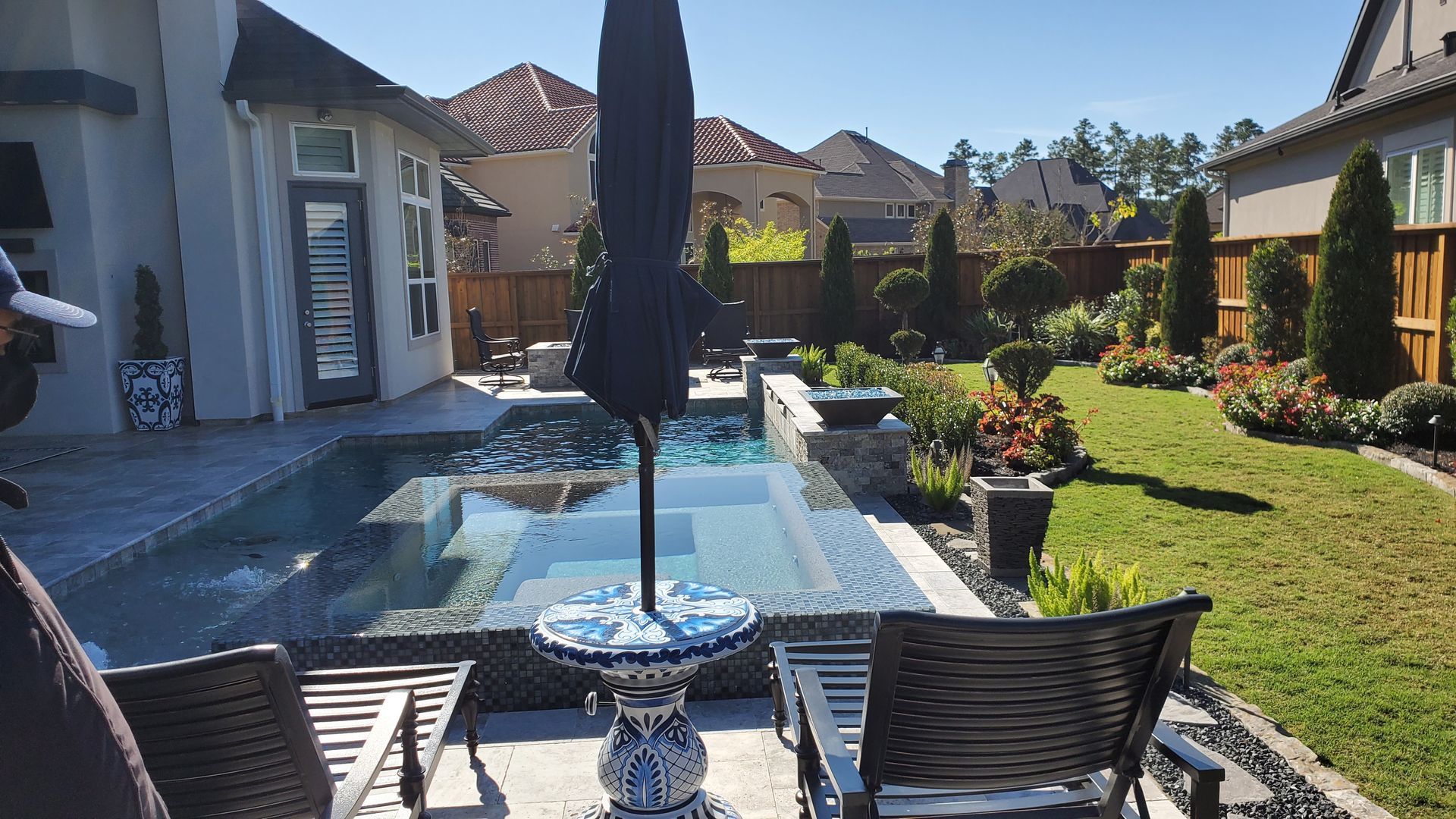 Backyard patio with pool, umbrella, chairs, and landscaped garden under bright sun
