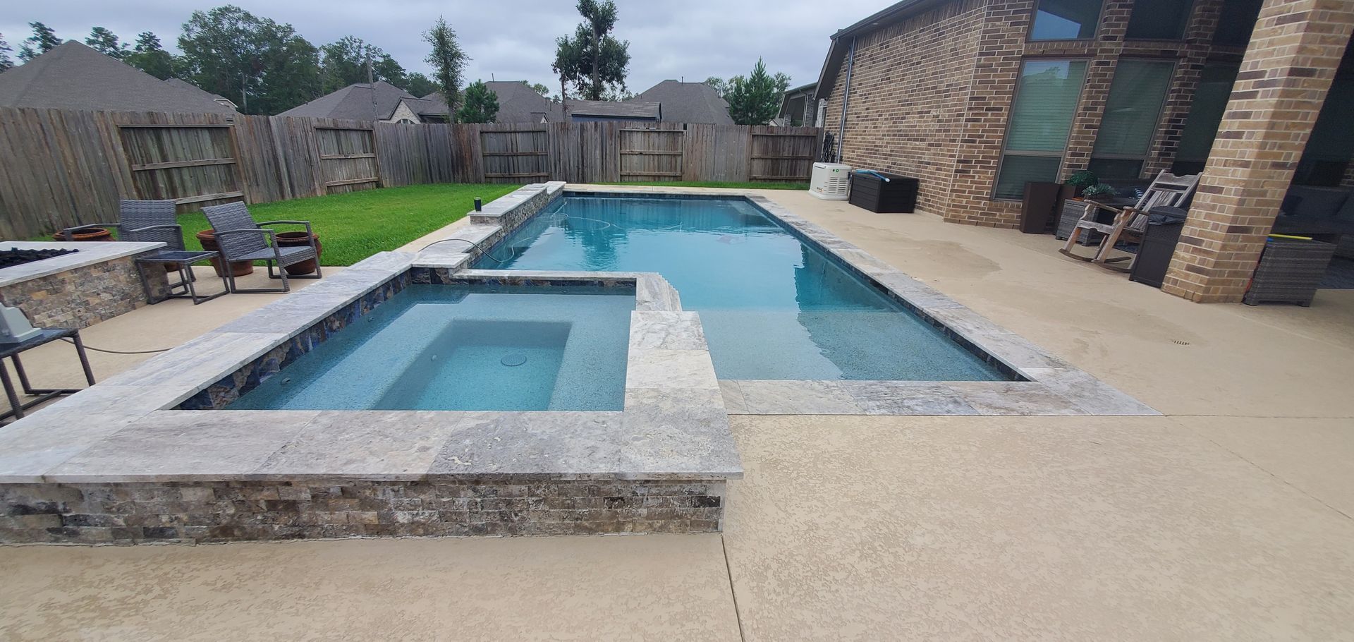 Backyard with a long swimming pool and attached hot tub beside a patio and stone house