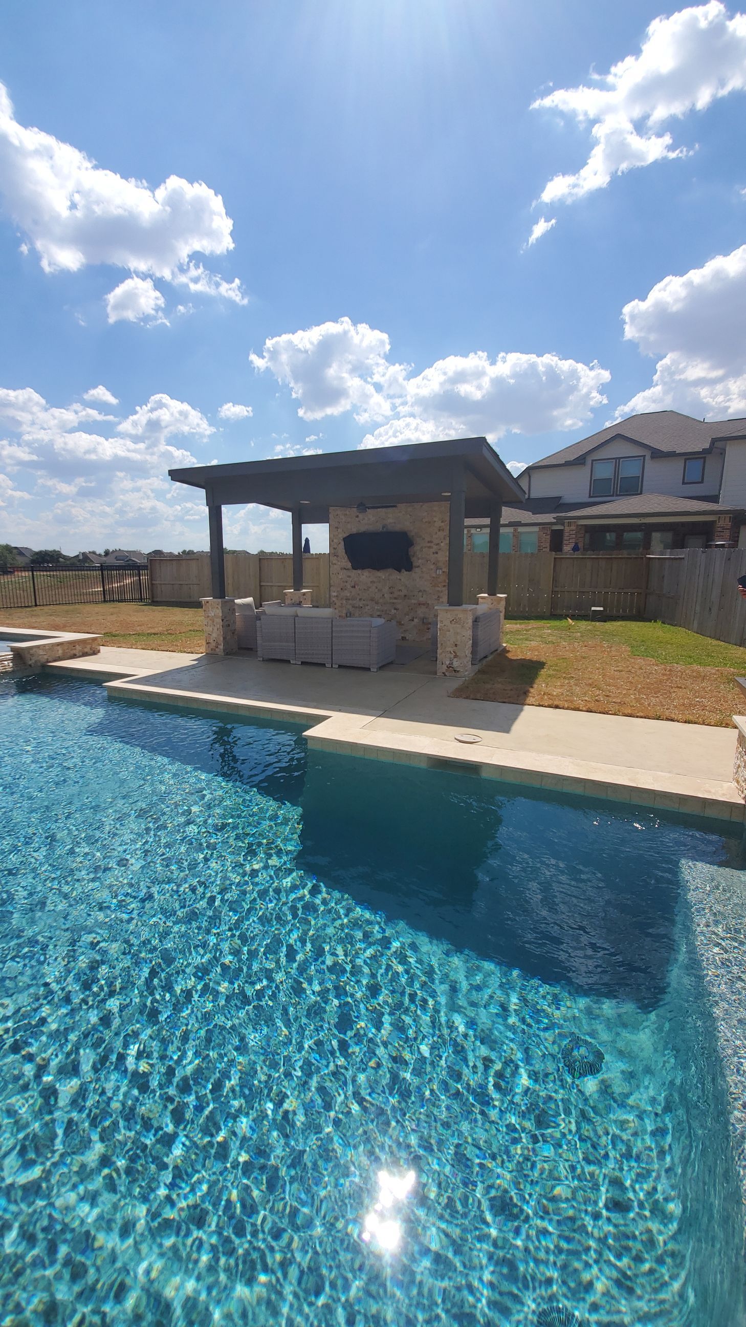 Blue swimming pool beside a stone cabana under a bright, partly cloudy sky.