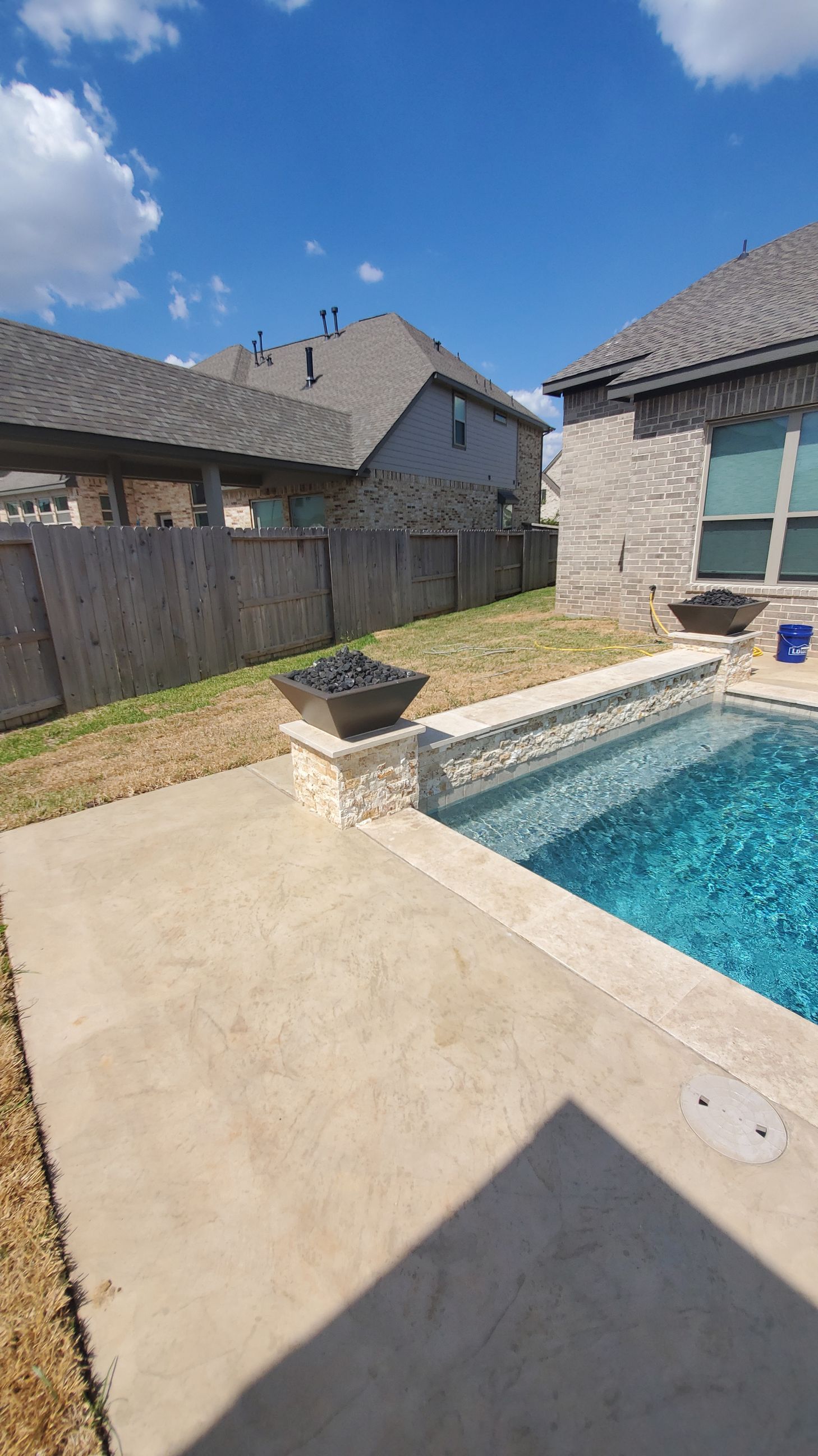 Backyard patio with a swimming pool, stone fire pit, and houses under a blue sky