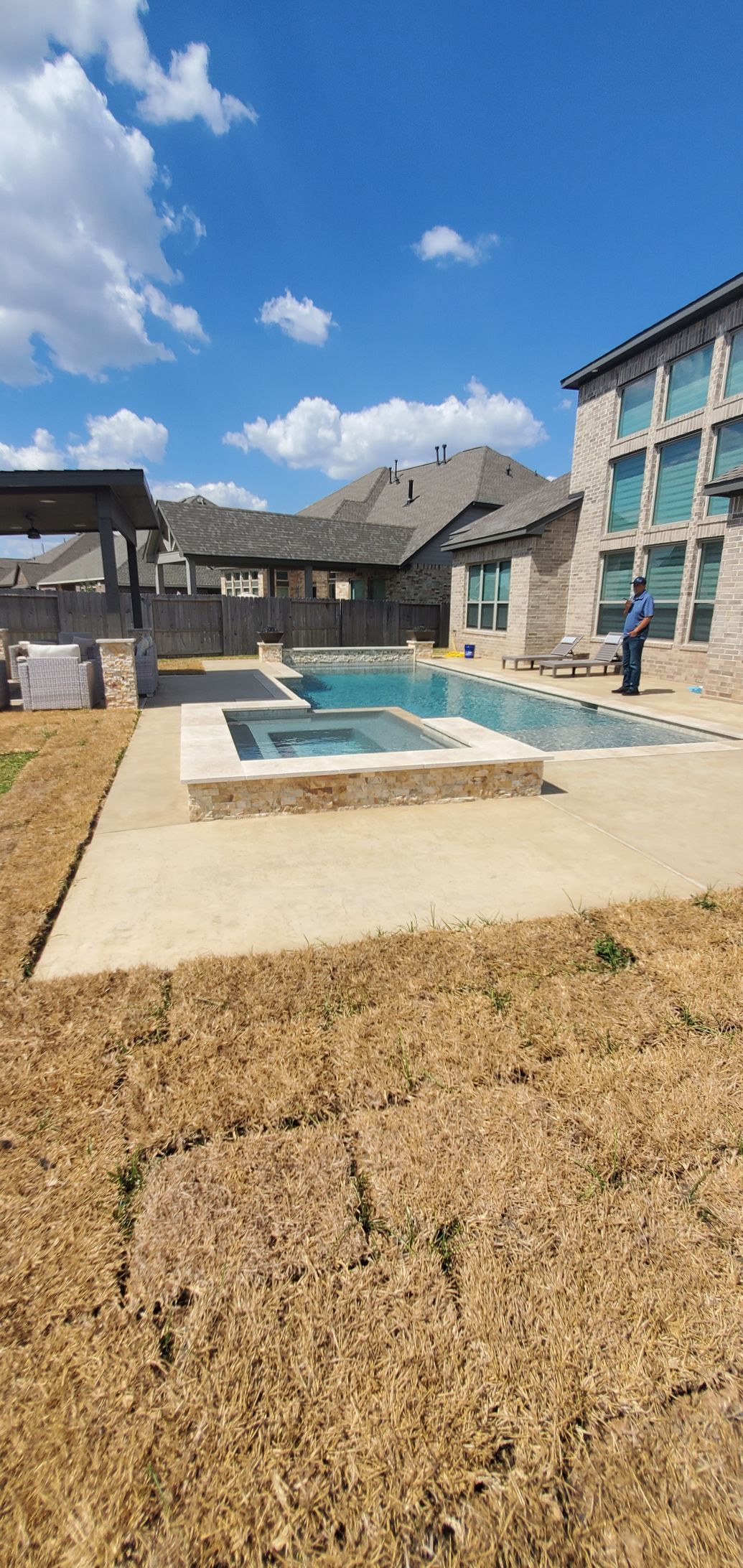Apartment courtyard with a blue pool, patio, and partly cloudy sky