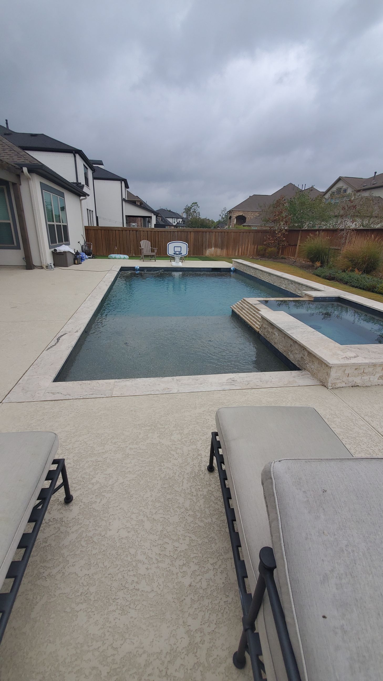 Backyard patio with rectangular pool, cloudy sky, and lounge chairs in the foreground