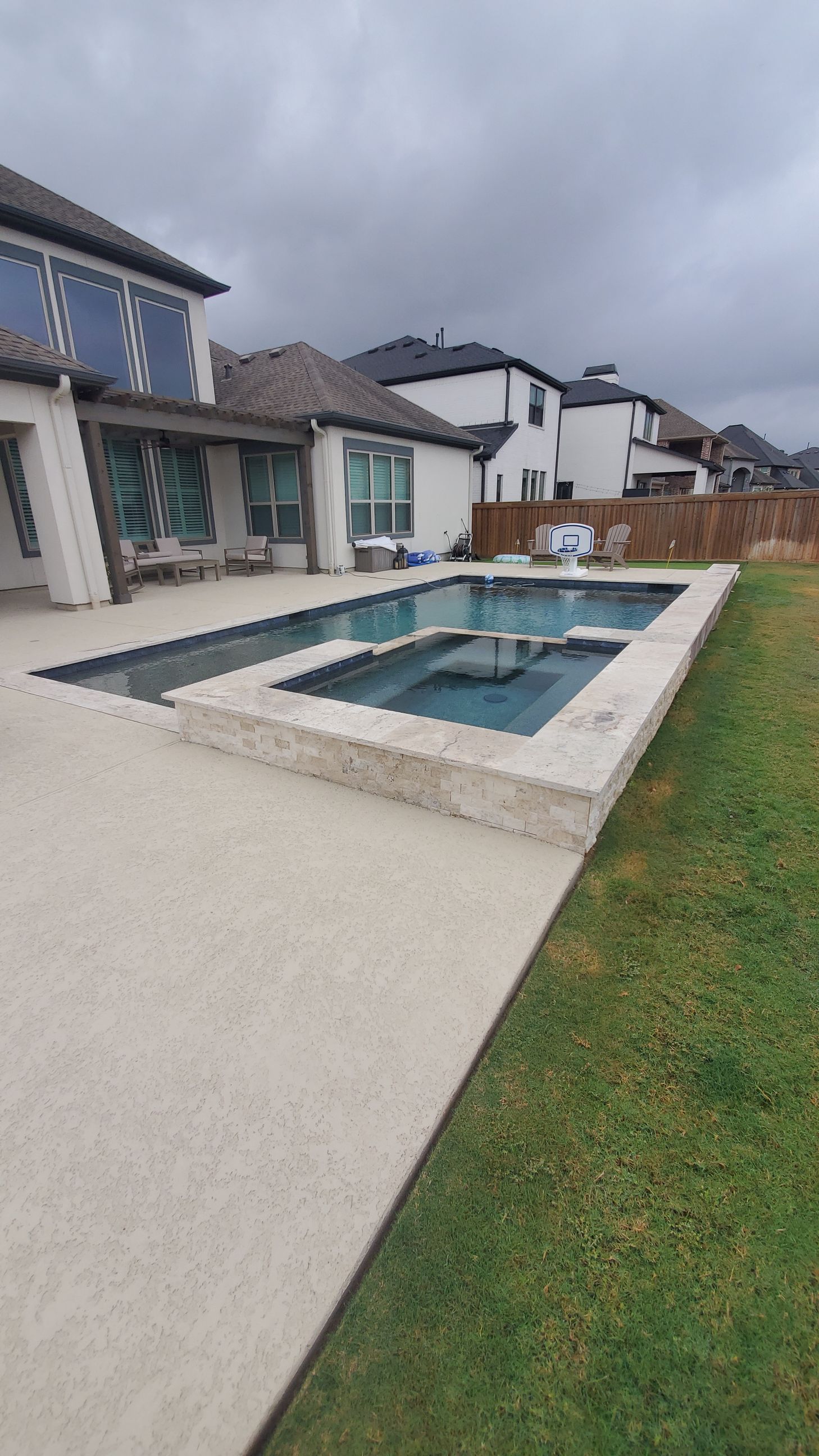 Backyard swimming pool beside a modern house and lawn under cloudy skies