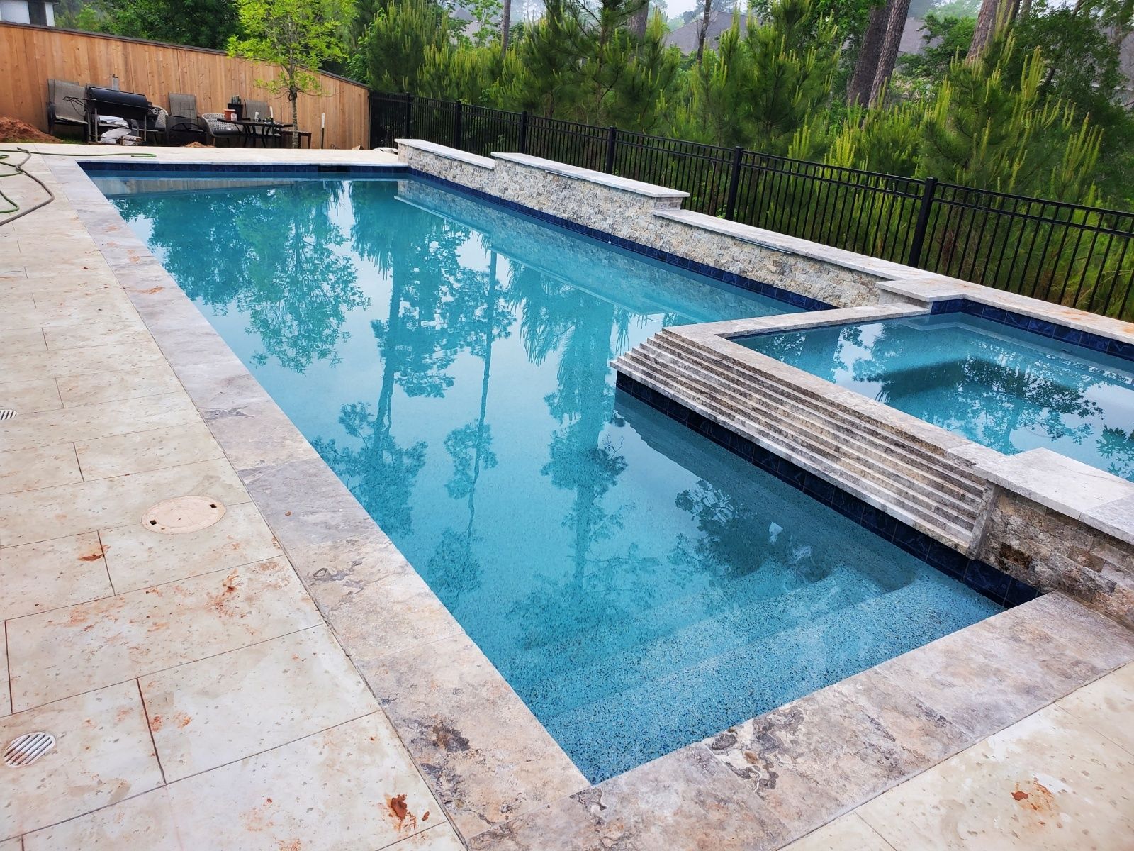 Backyard swimming pool with blue water, stone deck, and a raised hot tub surrounded by trees