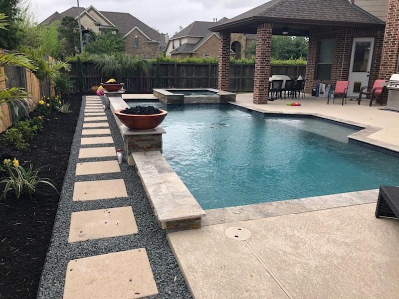 Backyard pool with stone deck, raised water feature, and covered patio seating area