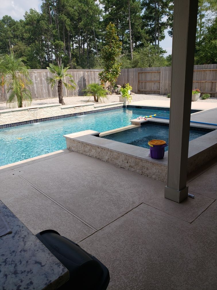 Backyard patio with a blue swimming pool, stone deck, and a covered seating area