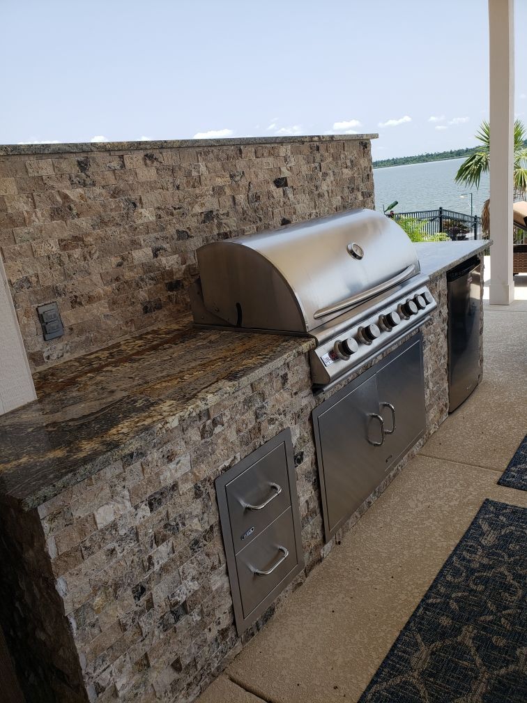 Outdoor stone patio with built-in stainless steel gas grill and countertop against a stone wall