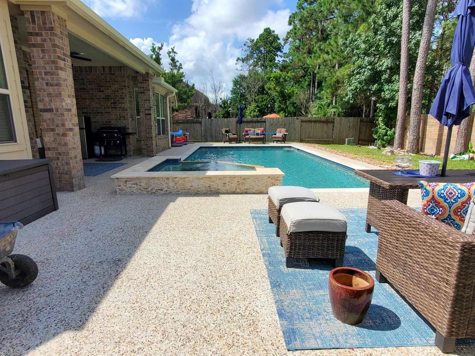 Backyard patio with a swimming pool, lounge chairs, and wicker seating on a sunny day