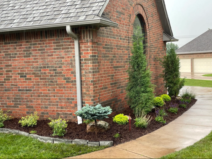 Brick house corner with landscaped flower beds and a curved concrete walkway