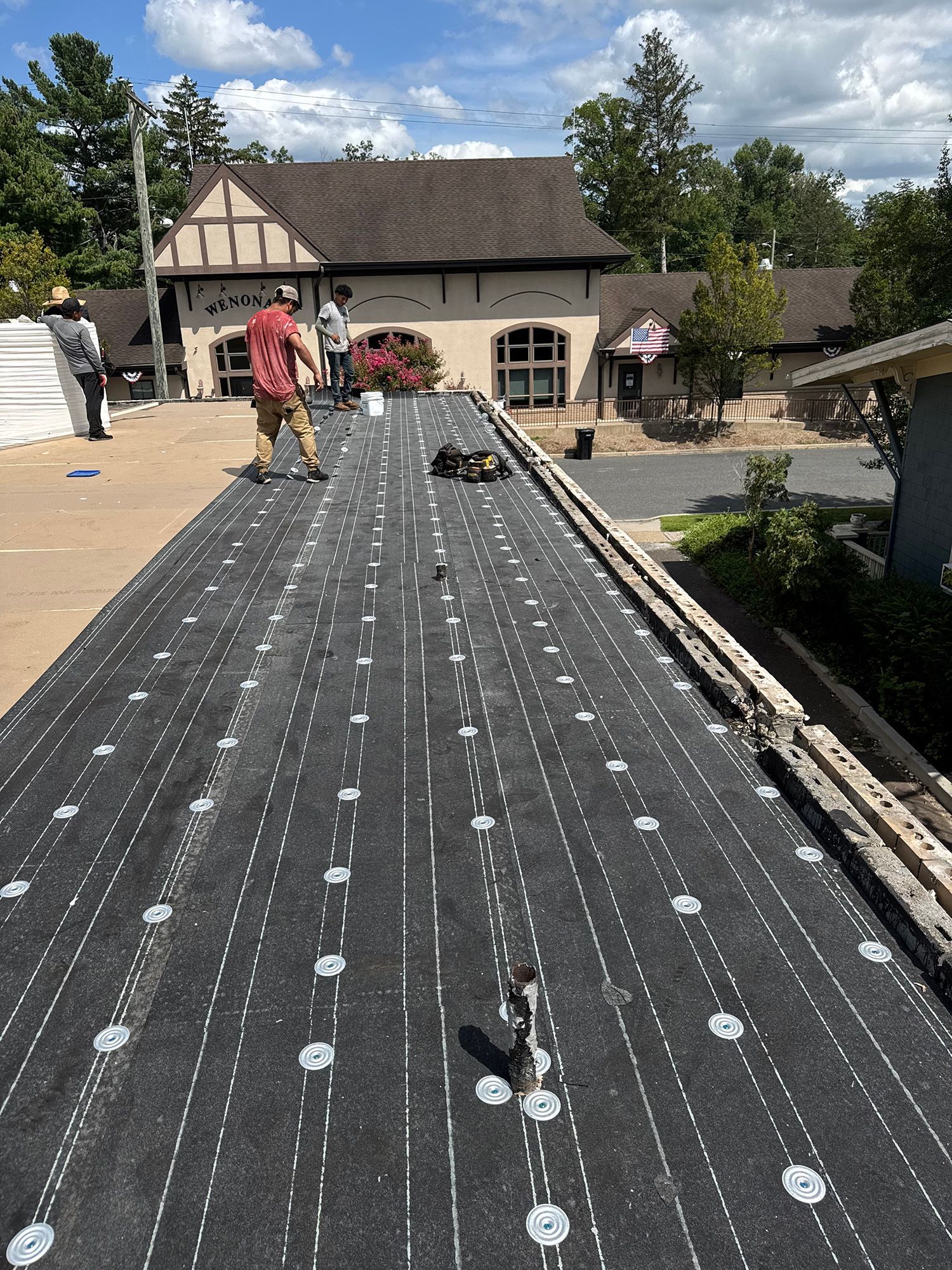 Roofers working on a flat roof, with a building in the background. Blue sky, sunny day.