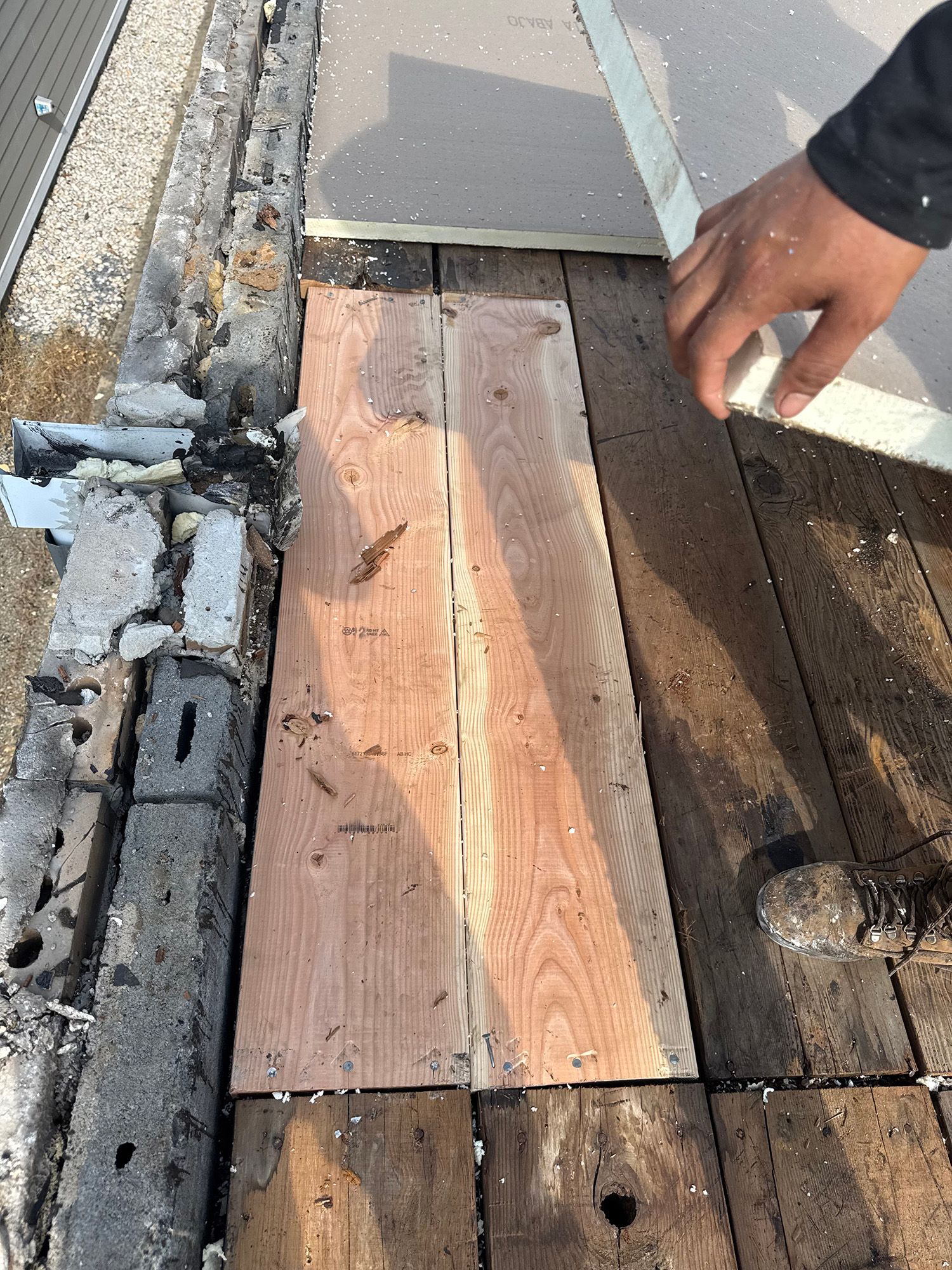 A person's hand touching wood planks on a roof, part of a repair.