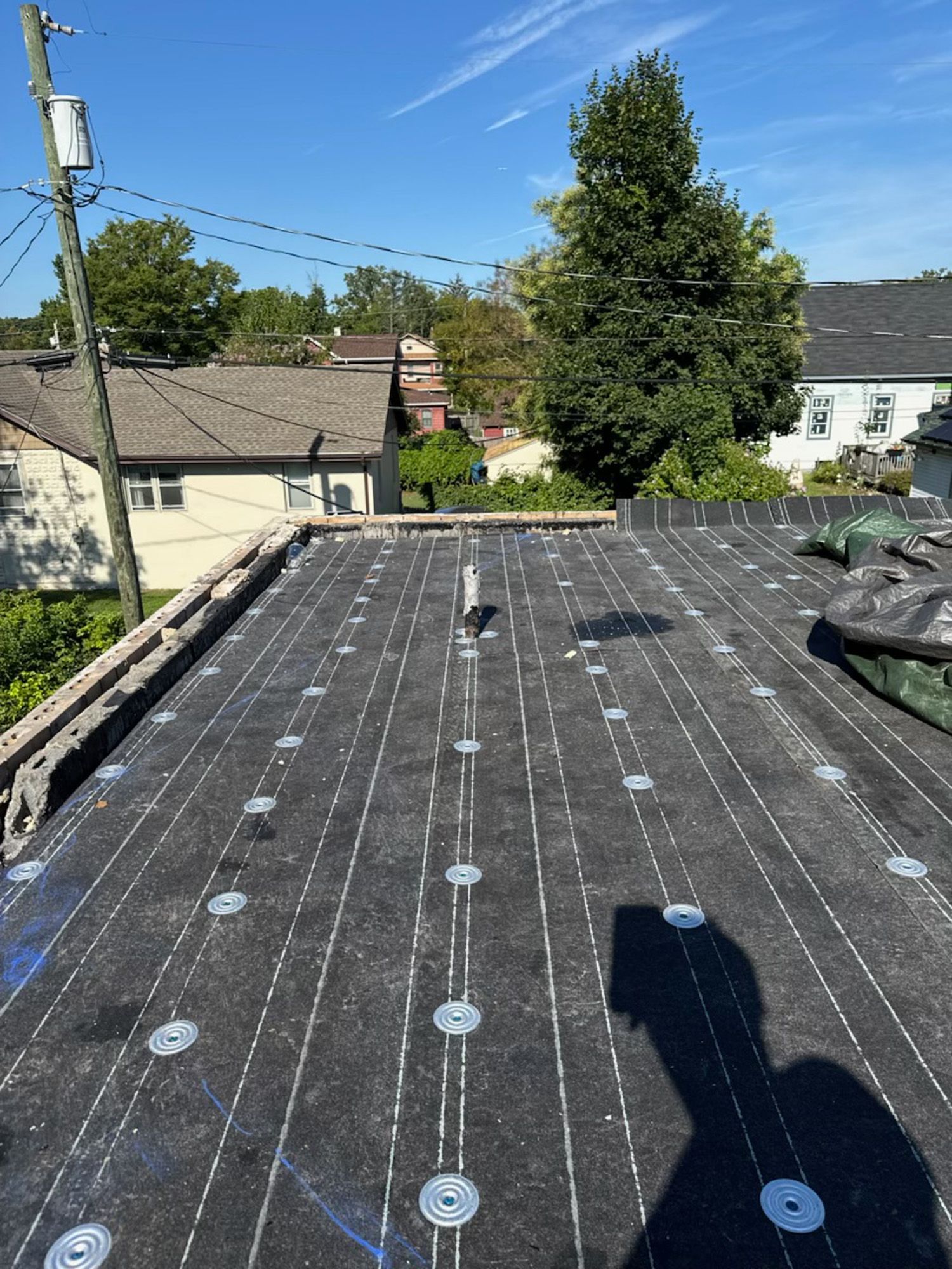 Flat roof with fasteners, vent pipe, and surrounding houses under a blue sky.