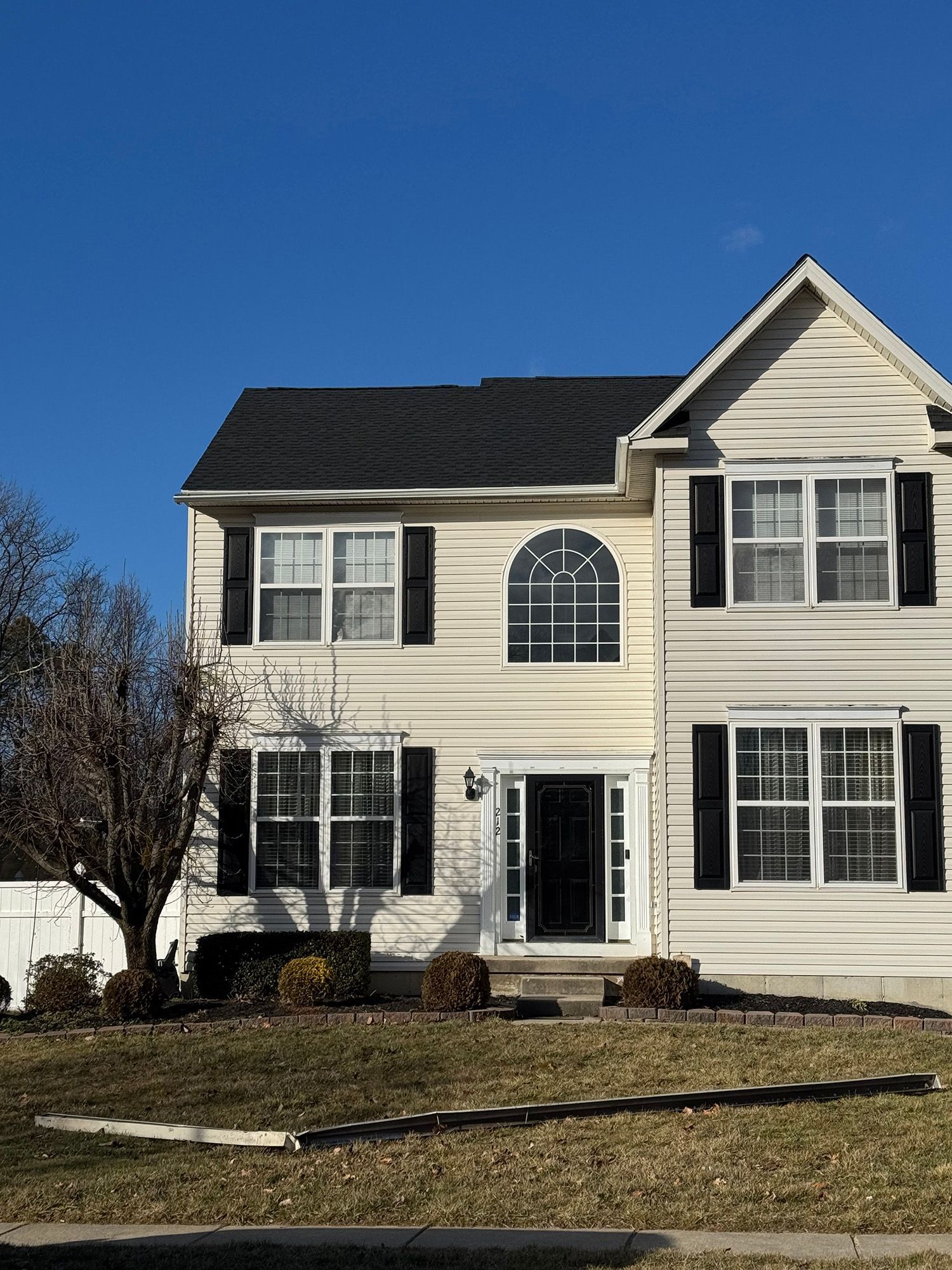 Two-story house with black shutters, black door, and arched window, set against a bright blue sky.
