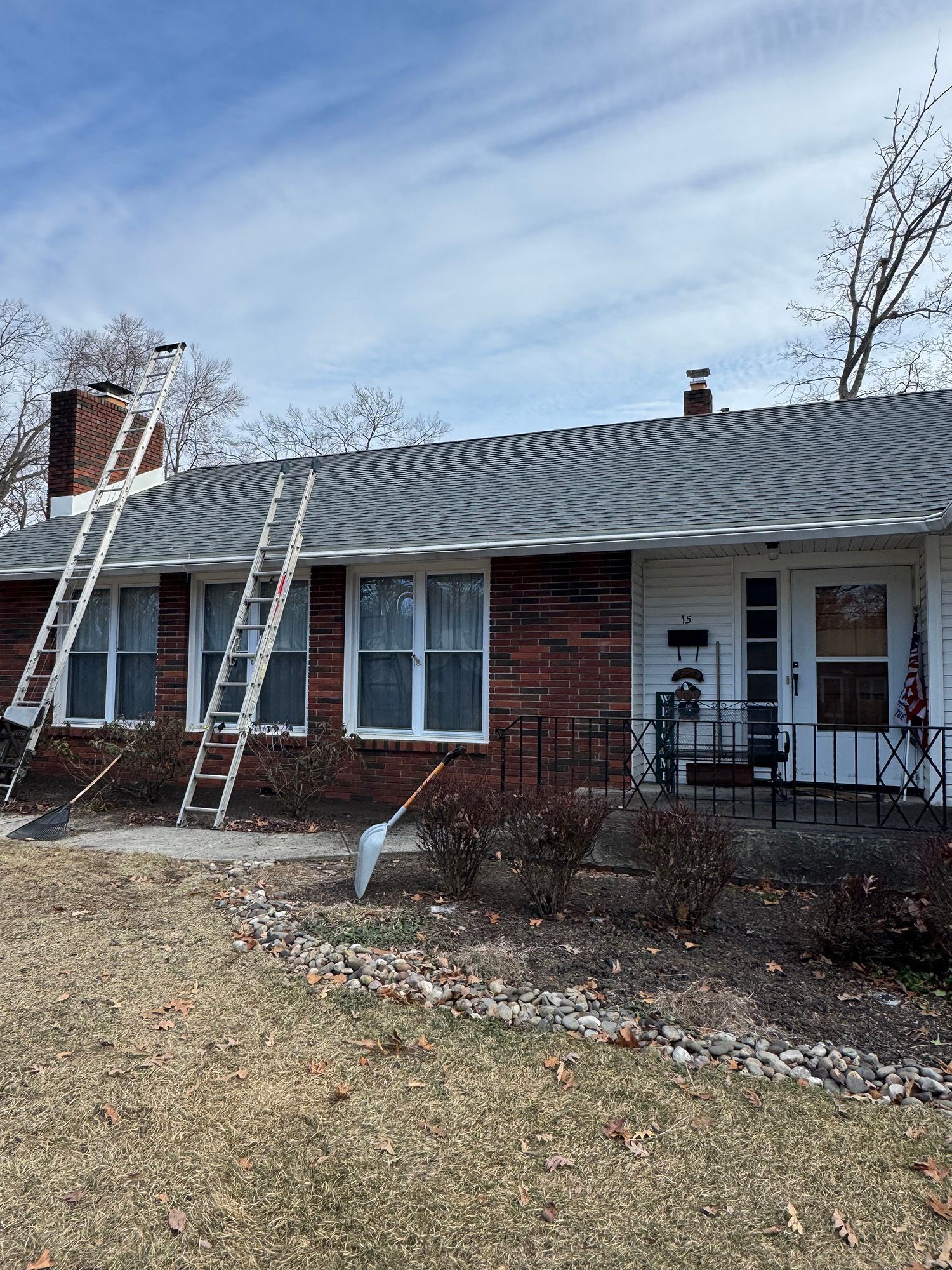 Ladder leaning against a house roof; brick exterior, cloudy sky.