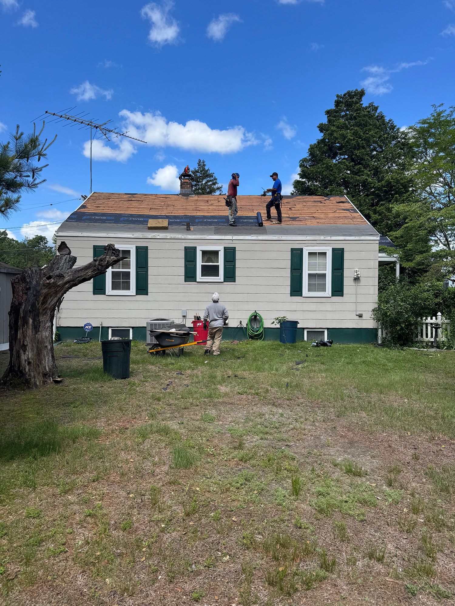 Roofers working on a house with visible missing shingles under a blue sky.