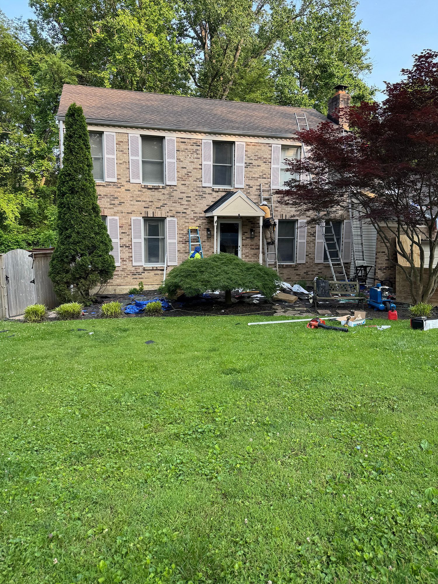 Stone house with two stories, white shutters, and a green lawn. People on ladders near the front door.